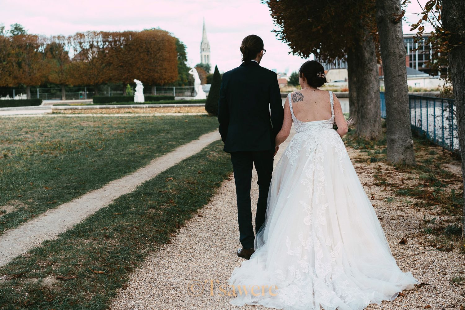 Bride and groom walking hand in hand through scenic park with church view in background.