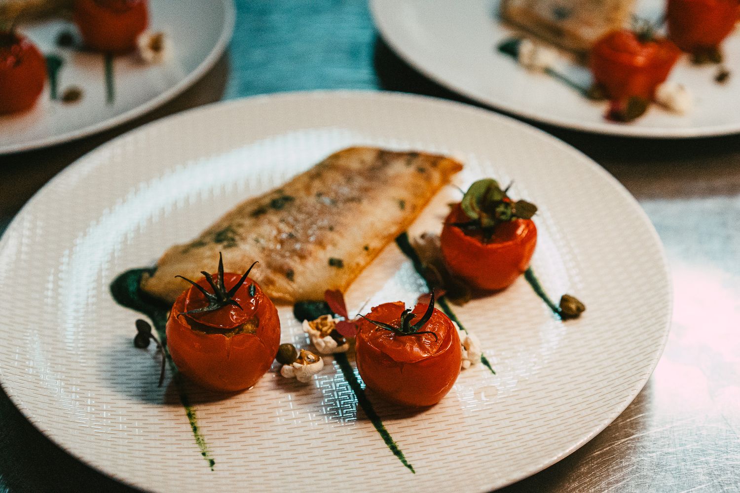 Grilled fish fillet served with roasted cherry tomatoes and capers on a white plate.