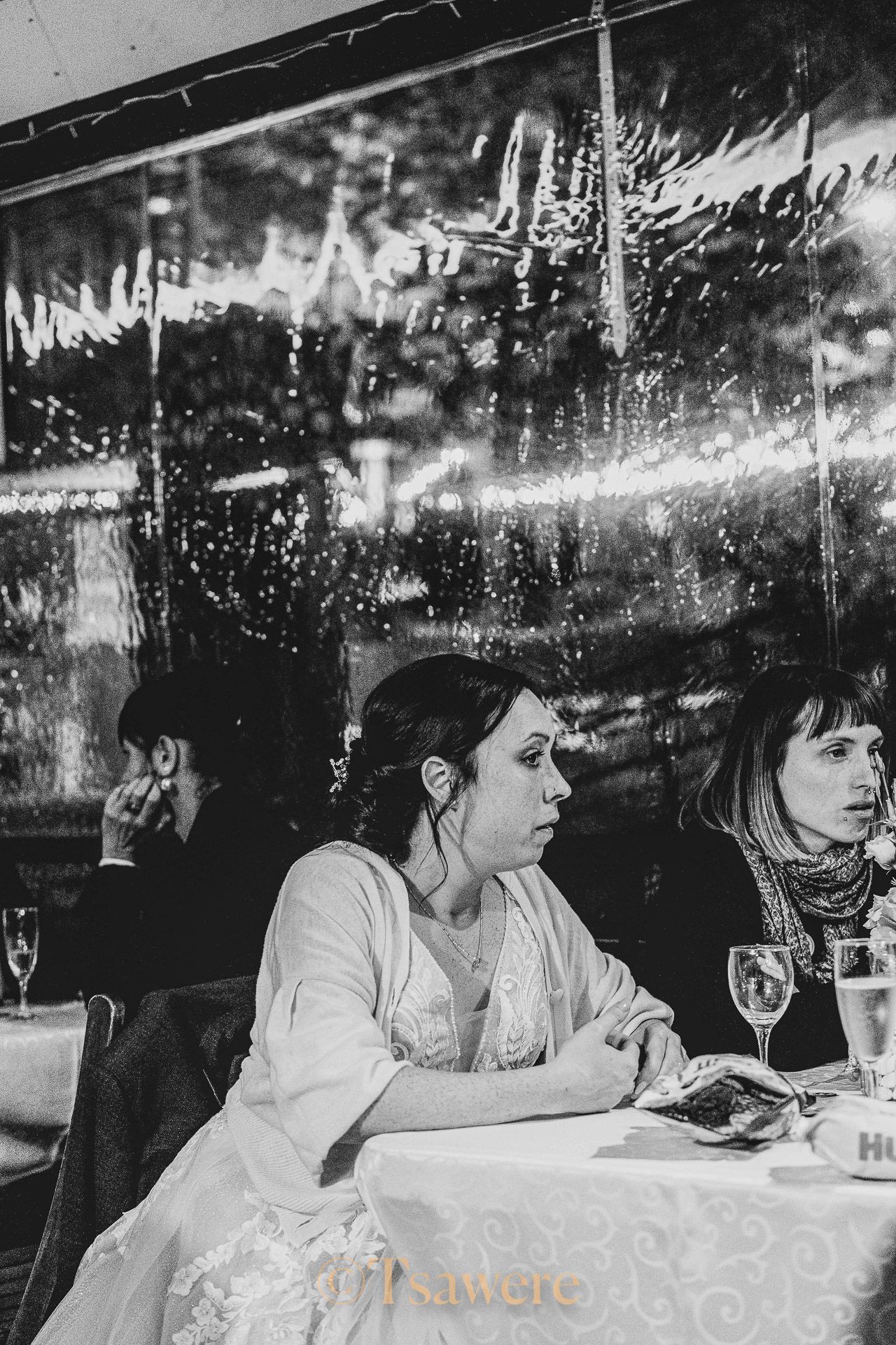 Bride in white dress seated at wedding reception table, black and white photo.