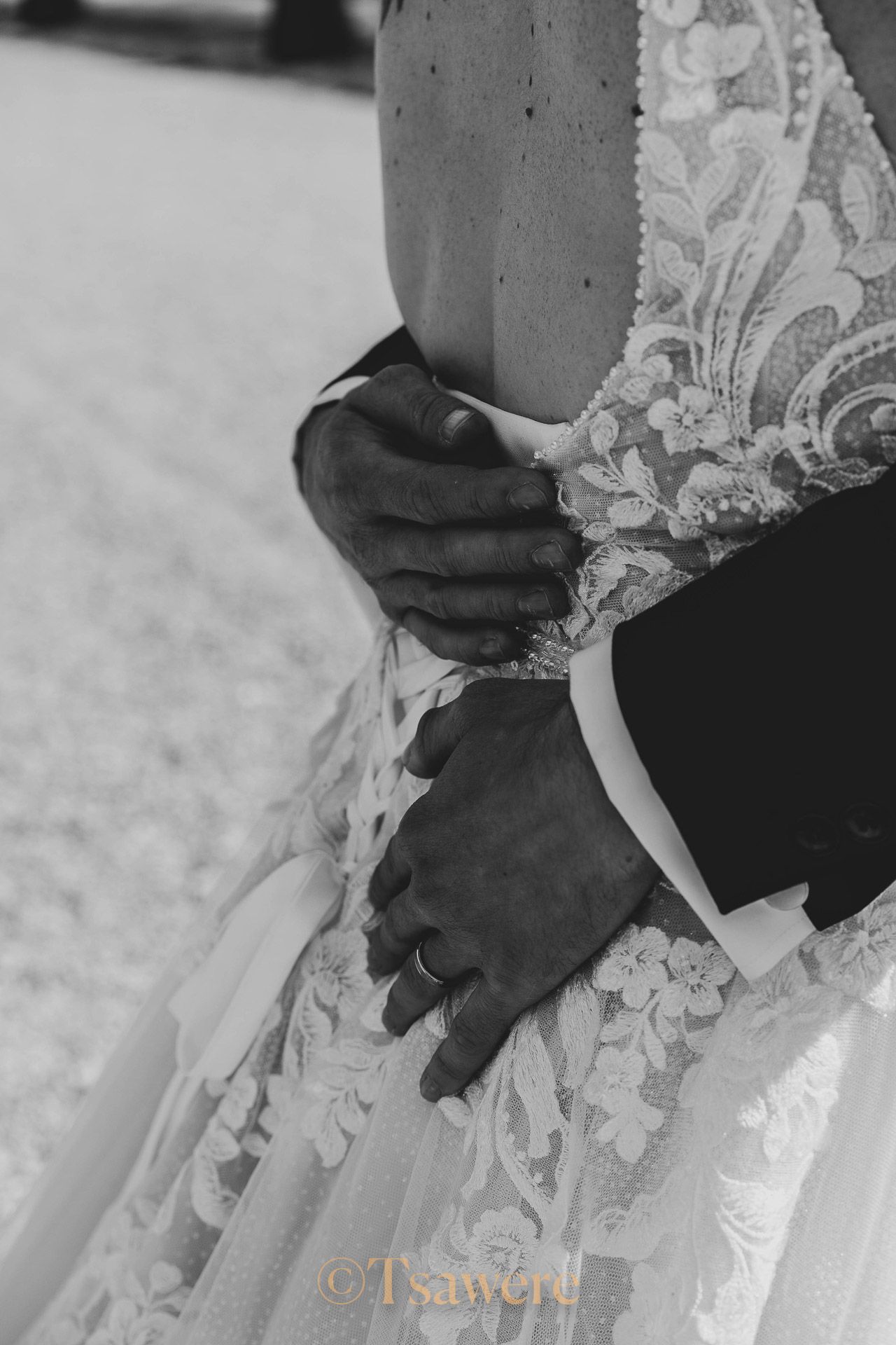 Black and white close-up of groom holding bride at the waist showcasing intricate lace wedding gown.