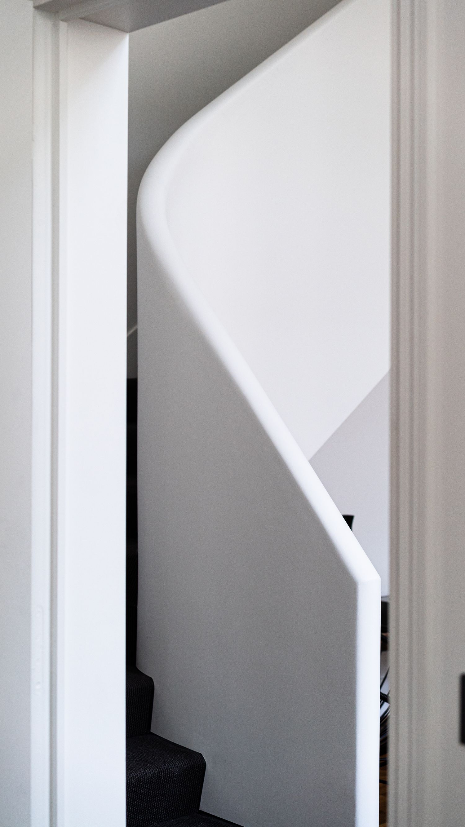 Minimalist white curved staircase with smooth sculptural banister viewed through a narrow doorway in a modern interior.