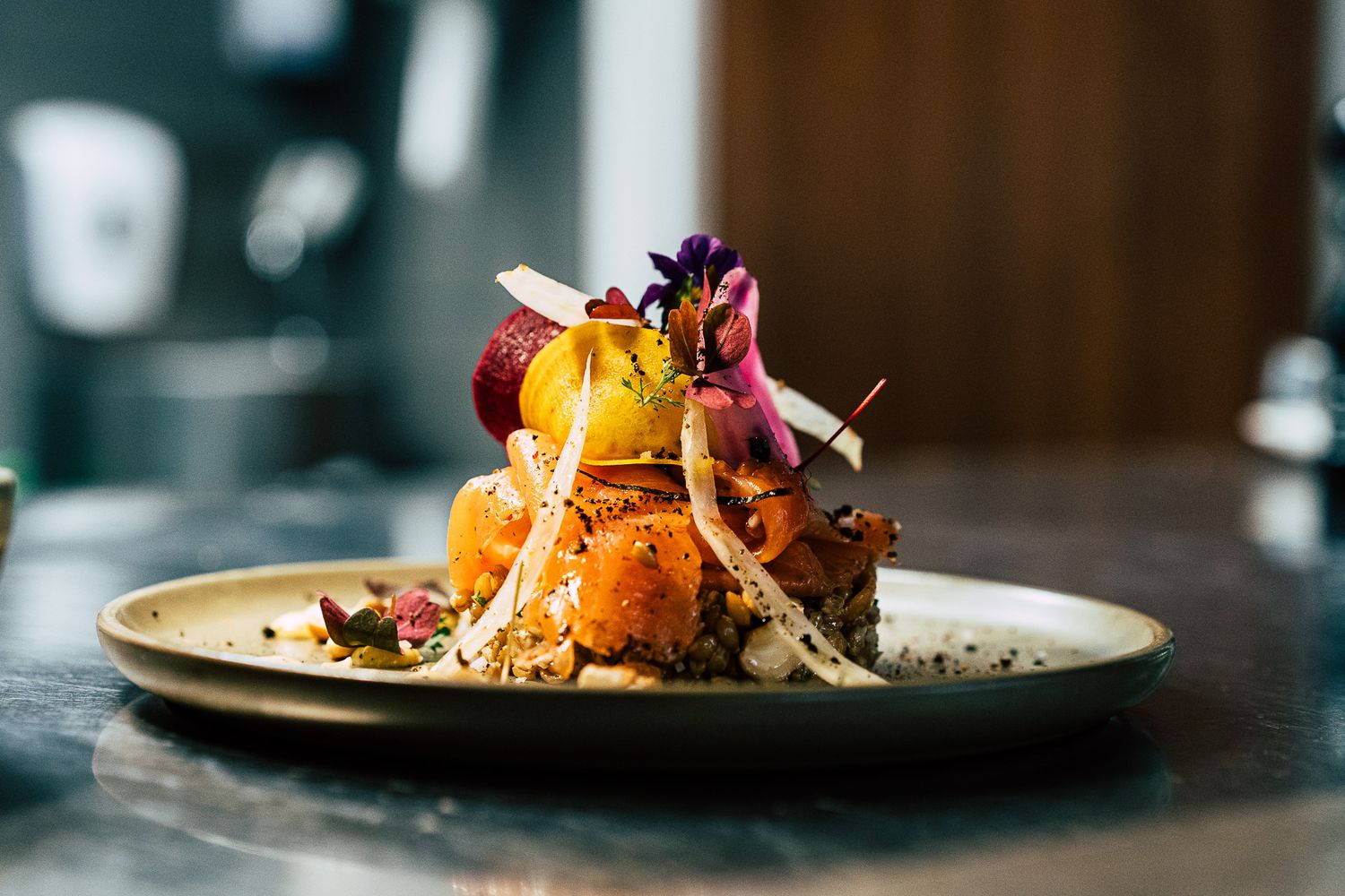 Elegantly plated gourmet dish with colorful vegetables, edible flowers, and garnishes stacked artfully on a ceramic plate.