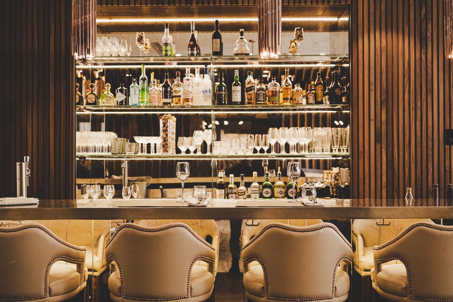 Glamorous bar at Odette restaurant with backlit shelves of premium spirits and cream chairs.