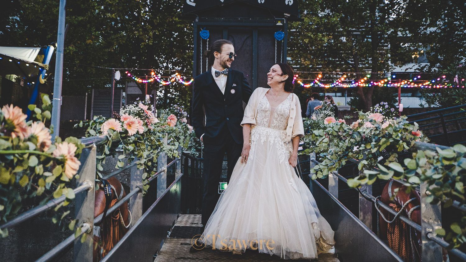 Bride and groom sharing romantic glance on decorated boat gangway with floral arrangements.