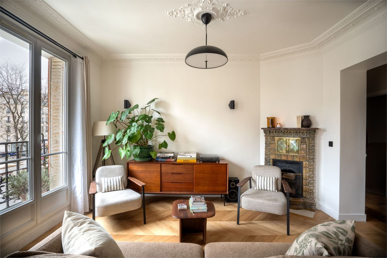 Cozy Parisian living room with mid-century furniture, brick fireplace, large windows, and vintage sideboard.
