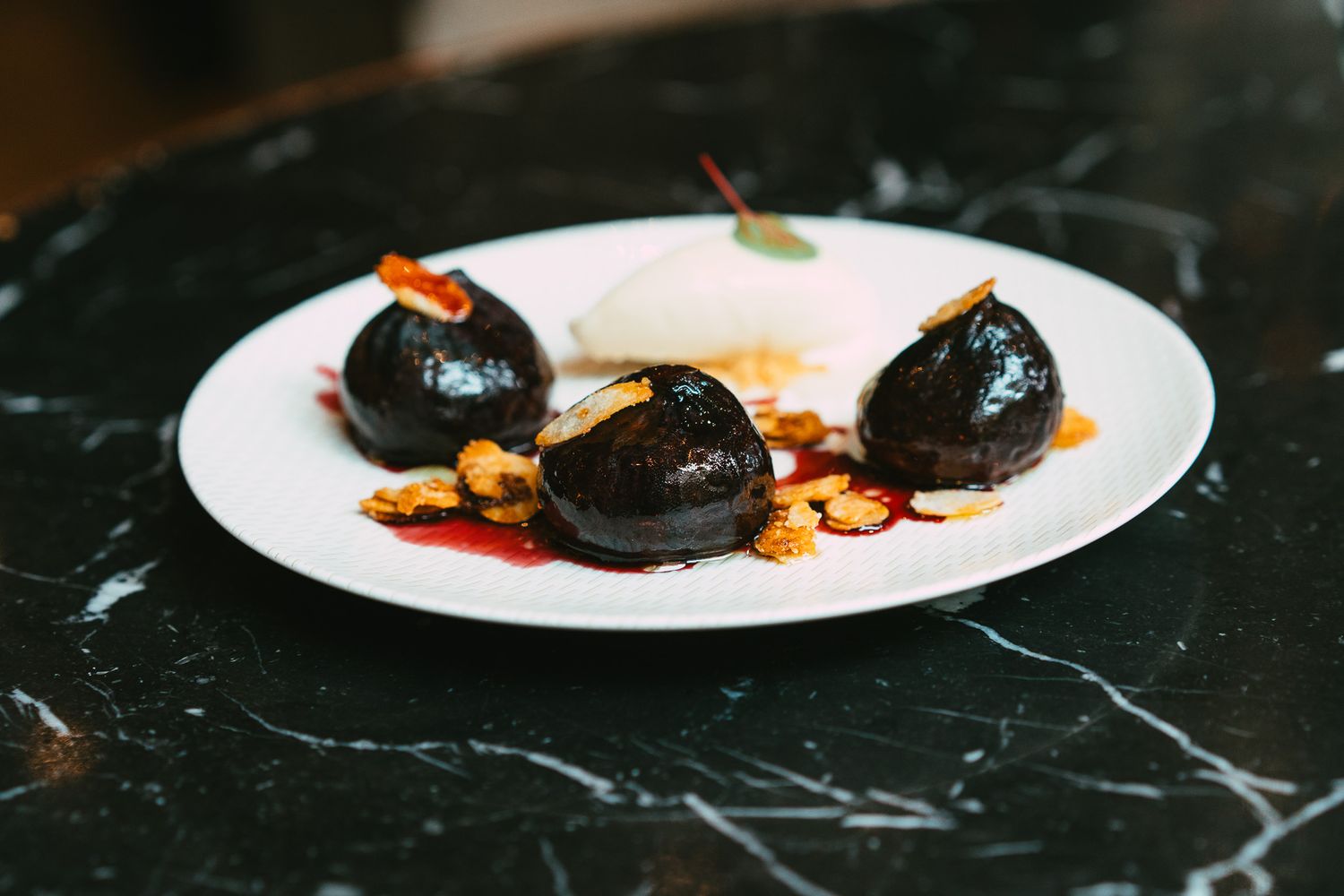 Three glazed chocolate dumplings with whipped cream and caramelized nuts on white plate.