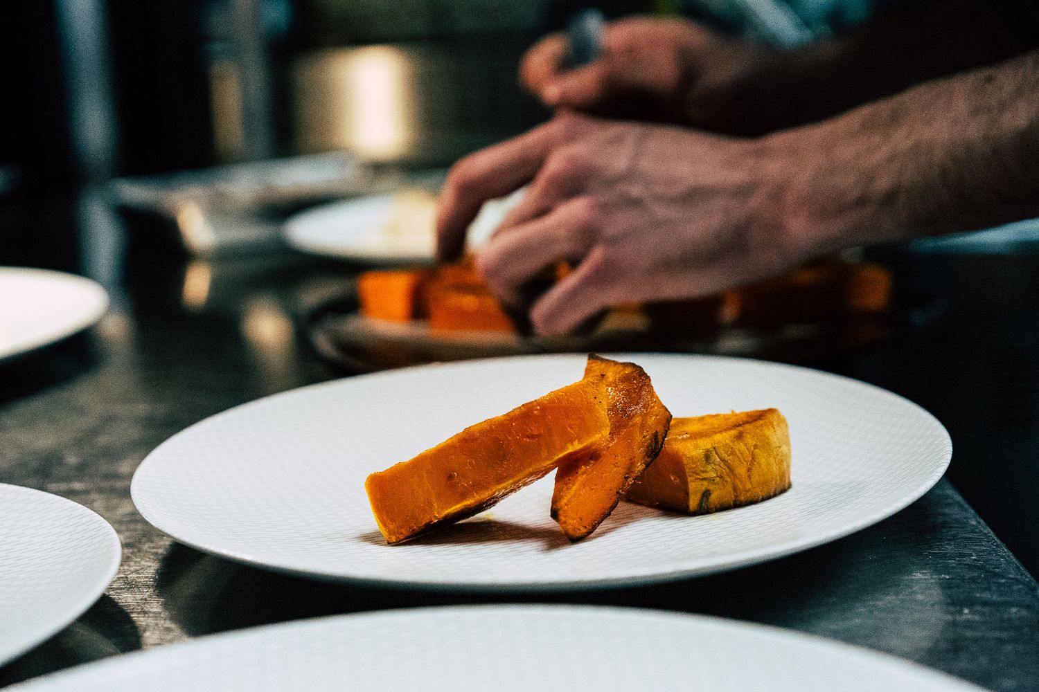 Roasted butternut squash pieces plated on a white dish in a professional kitchen.