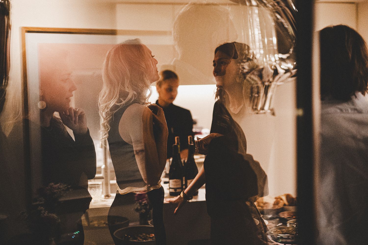 Warm-toned photo of elegantly dressed guests socializing at an indoor party.
