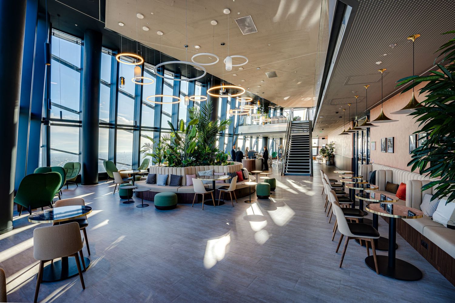Spacious modern lobby with floor-to-ceiling windows, lush plants, pendant lights, and stylish seating areas.