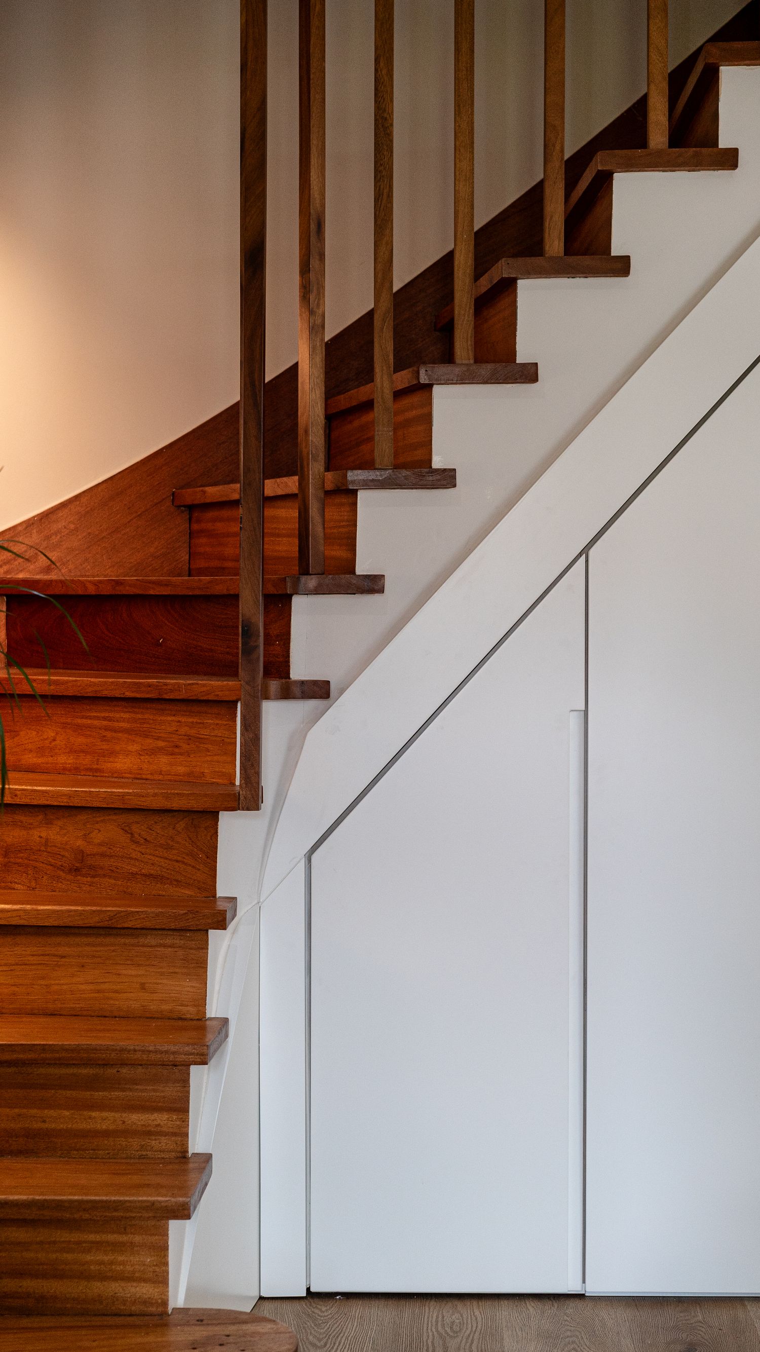 Classic wooden staircase with rich walnut treads, vertical balusters, and smart under-stair white storage cupboard.