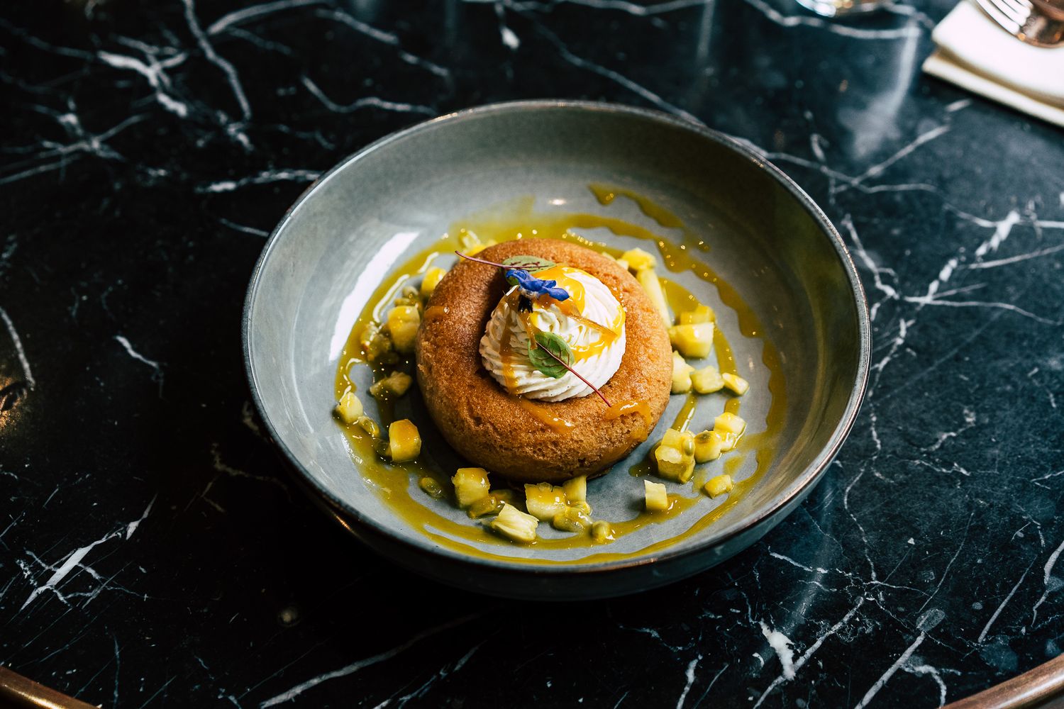 Gourmet breaded dish with corn and sauce served in a gray bowl on a black marble table.