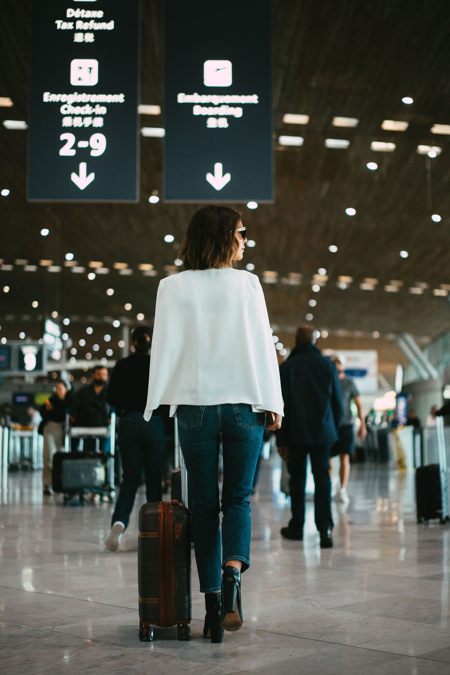 Stylish woman with luggage walking through an international airport terminal.