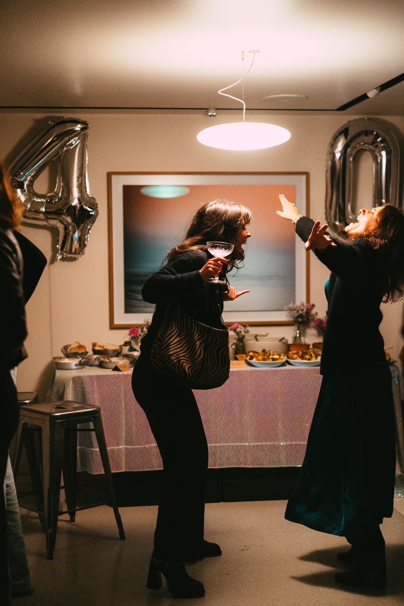 Women dancing and celebrating at a 40th birthday party with silver number balloons.