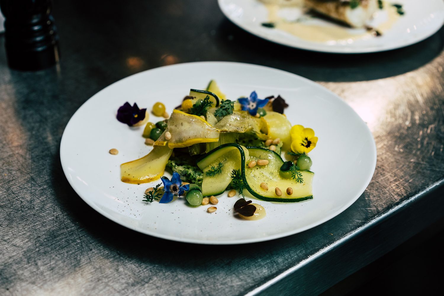 Delicate white fish fillet with zucchini ribbons, blue borage flowers, and yellow blooms on a white plate.