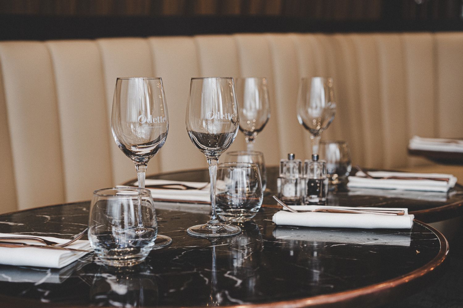 Multiple wine and water glasses arranged on a dark marble table in an upscale restaurant.