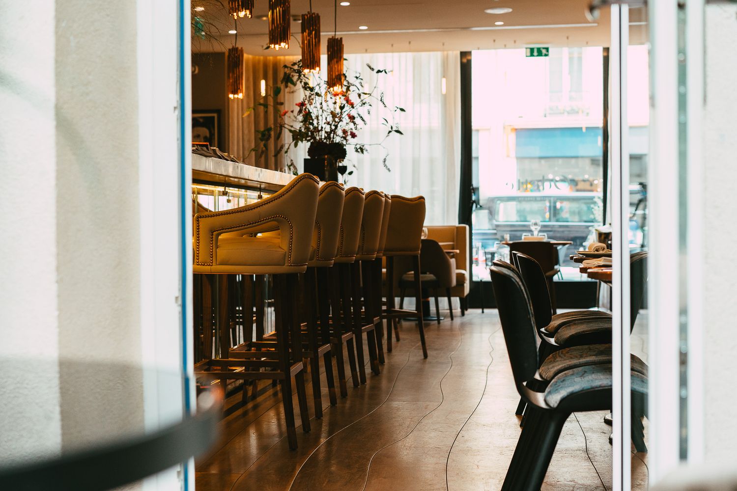A view through glass doors of an elegant restaurant interior with bar seating and warm lighting.