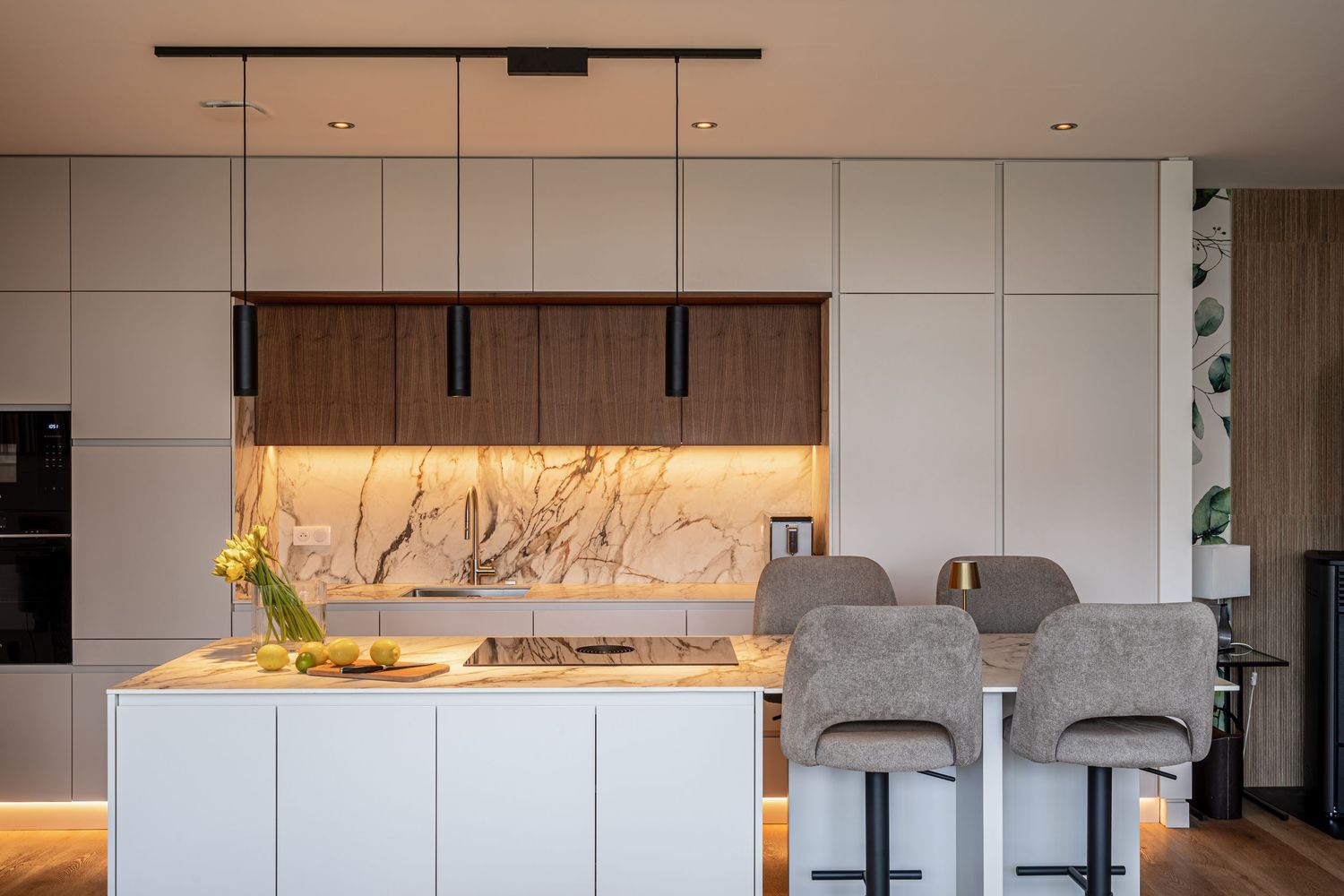 Sleek modern kitchen with white cabinetry, walnut accents, marble backsplash, island, and pendant lighting over bar stools.