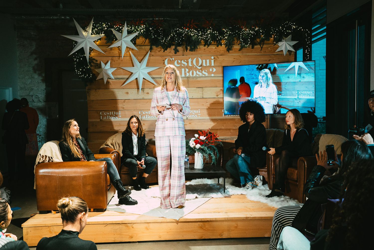 Woman in pink suit speaking on stage at a C'est Qui La Boss event with star decorations.