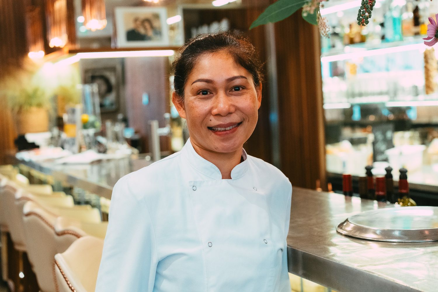 Smiling female chef in white uniform posing in an elegant restaurant with soft ambient lighting.