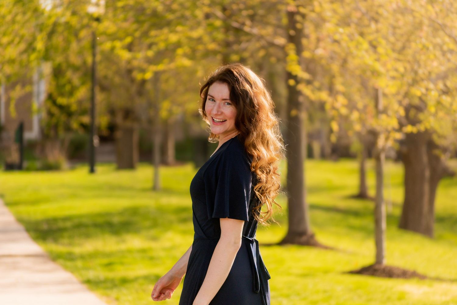 Woman walking through sunny park with trees in springtime.