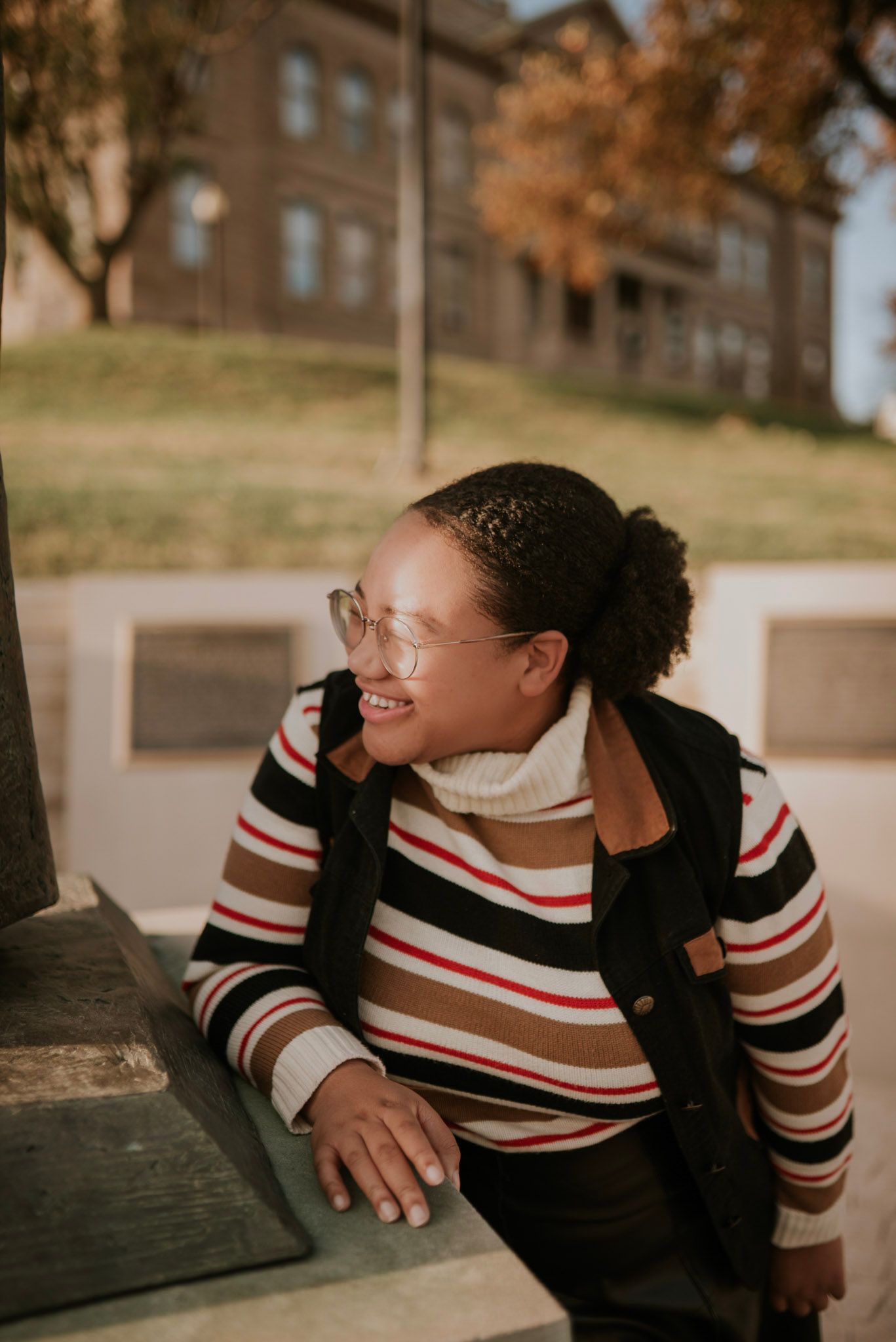 A person in a striped sweater laughing joyfully outdoors during autumn.