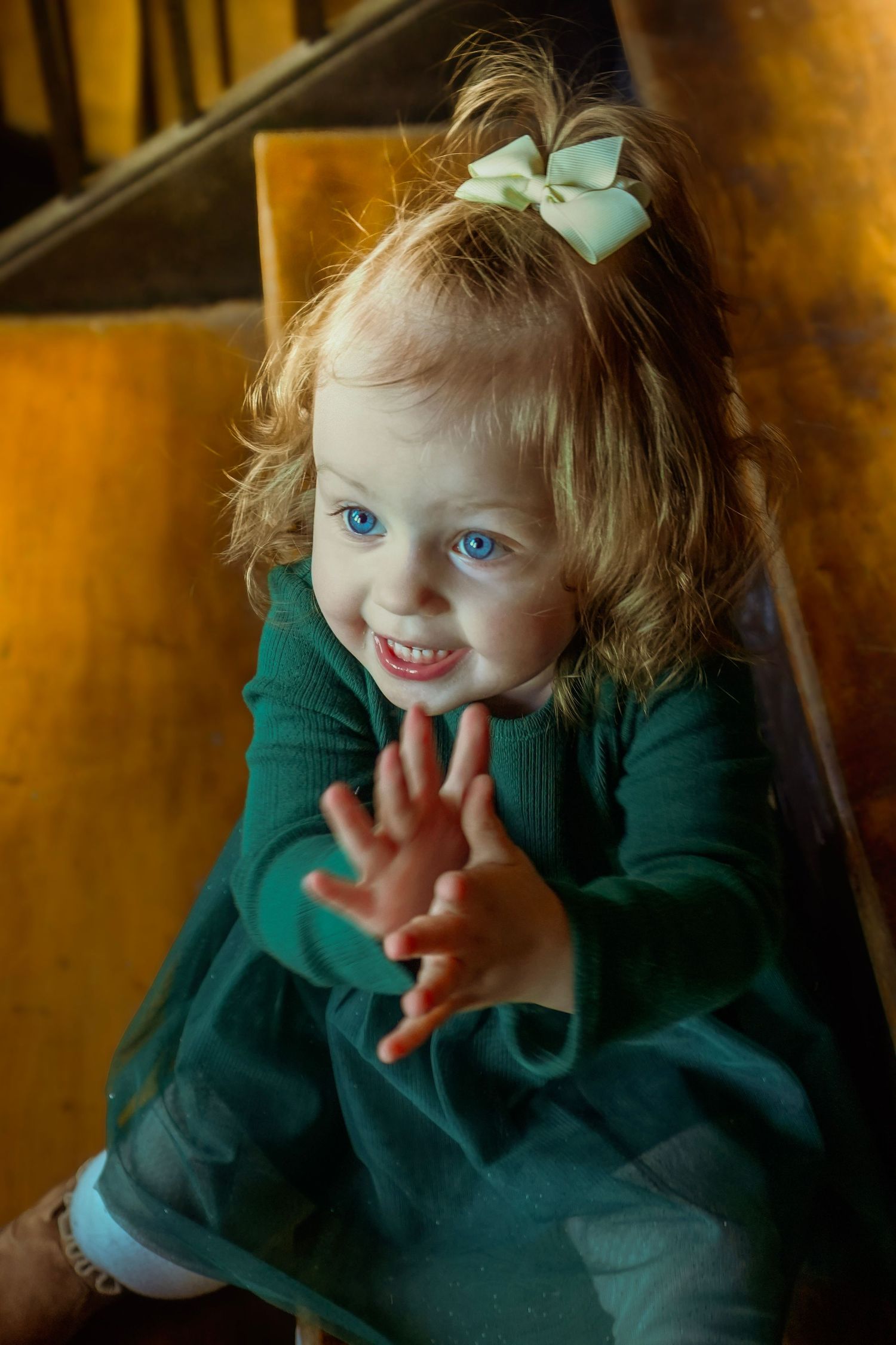 Child in green clothing making playful expressions and gestures.
