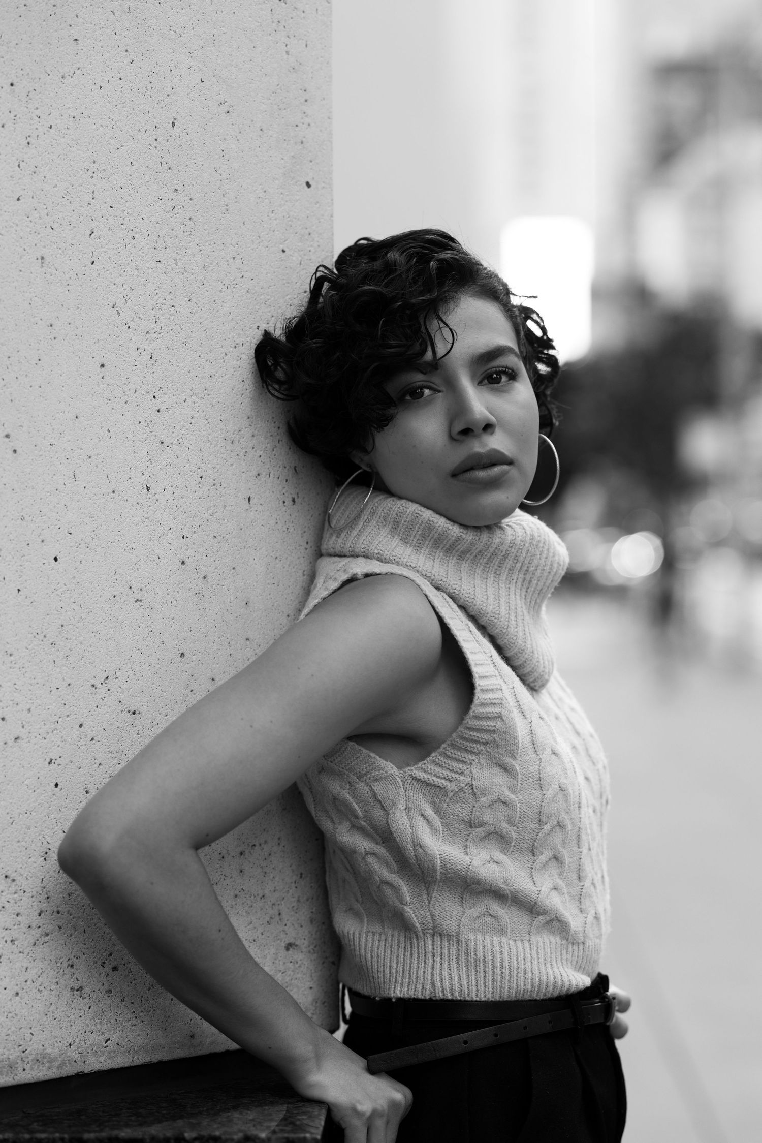 A black and white photo series shows a figure in a white top and dark bottoms posing against a textured wall.