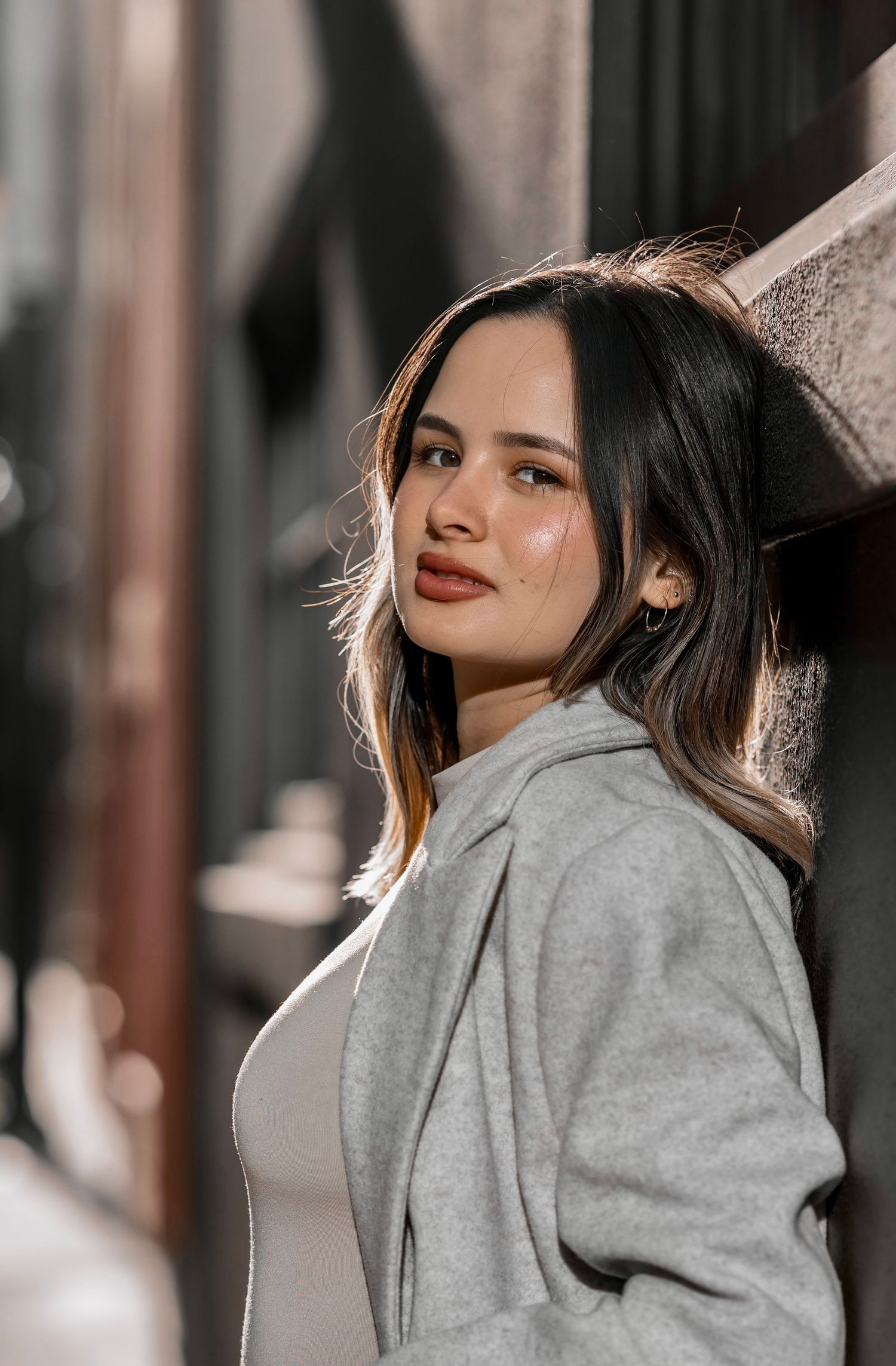 Portrait of a person in a gray coat looking over their shoulder with dramatic lighting and soft focus background.
