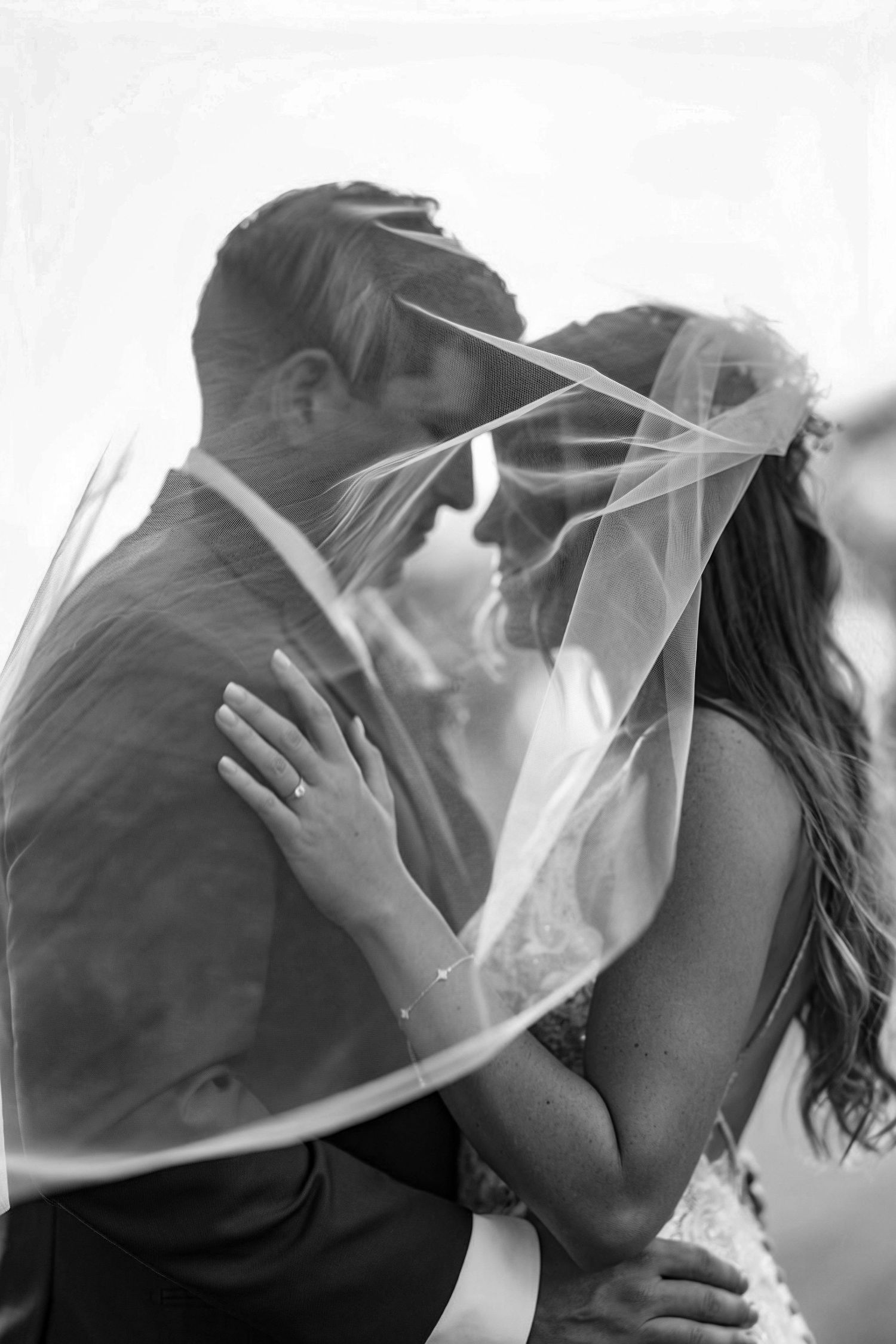 A romantic black and white photo series showing a couple sharing tender kisses under a wedding veil.