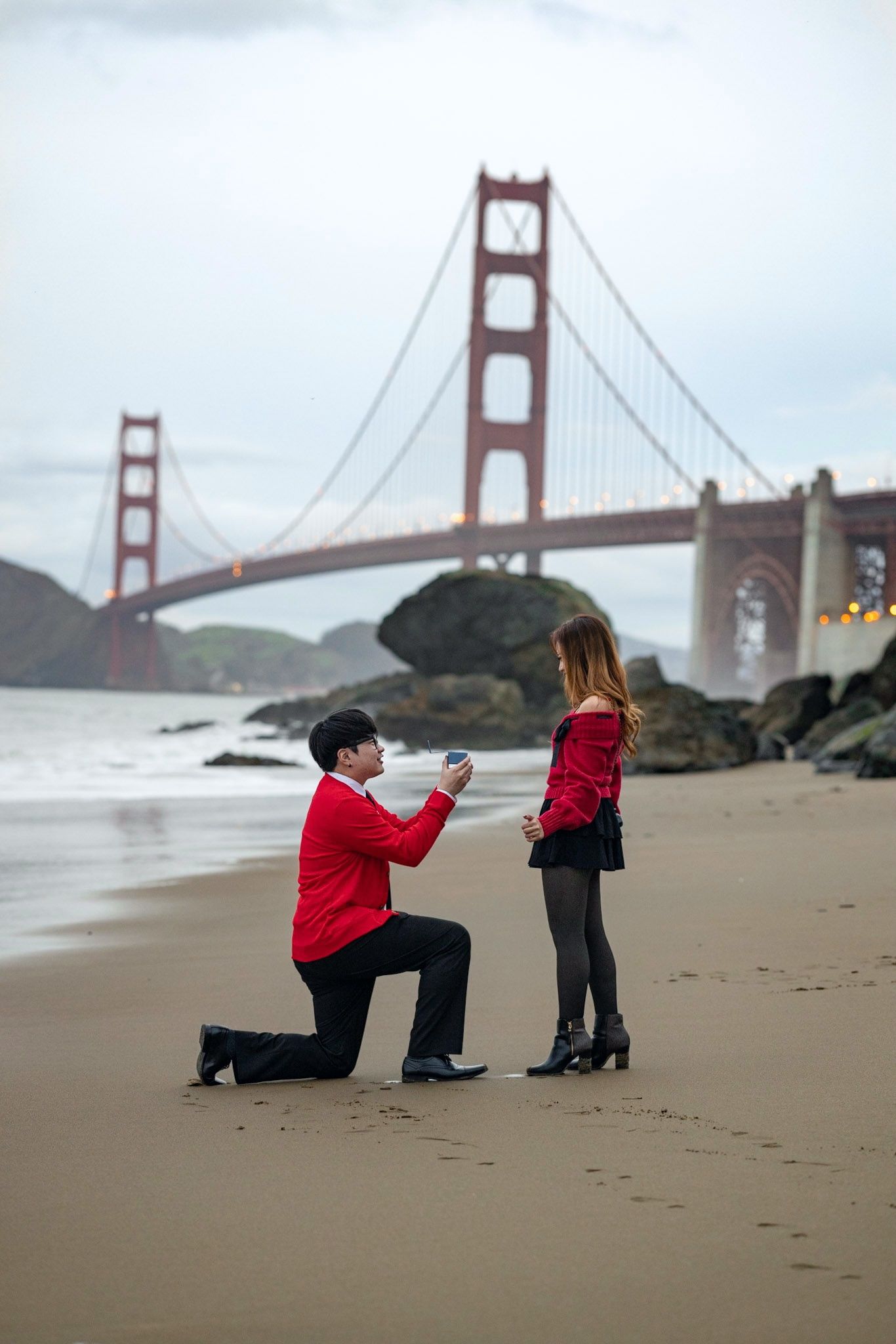 A romantic proposal moment on Baker Beach with the iconic Golden Gate Bridge in San Francisco creating a stunning backdrop.