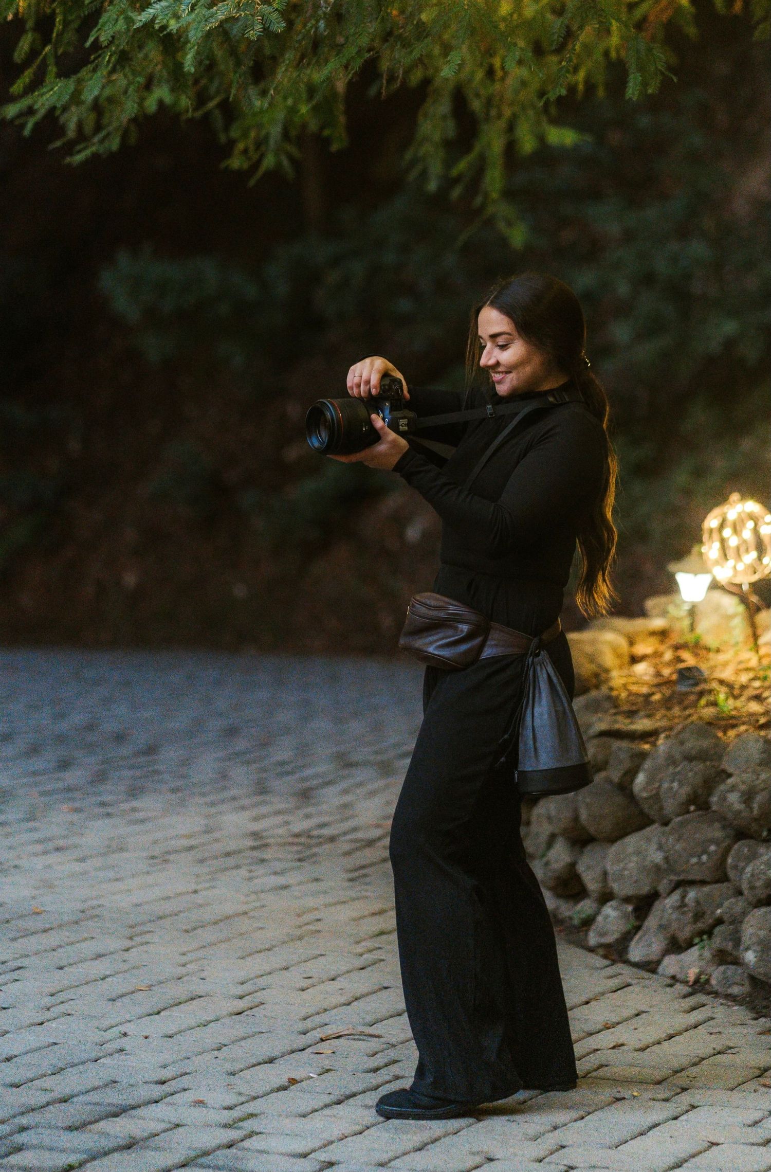 A person in a long black dress dances gracefully on a stone pathway at sunset taking a photo.