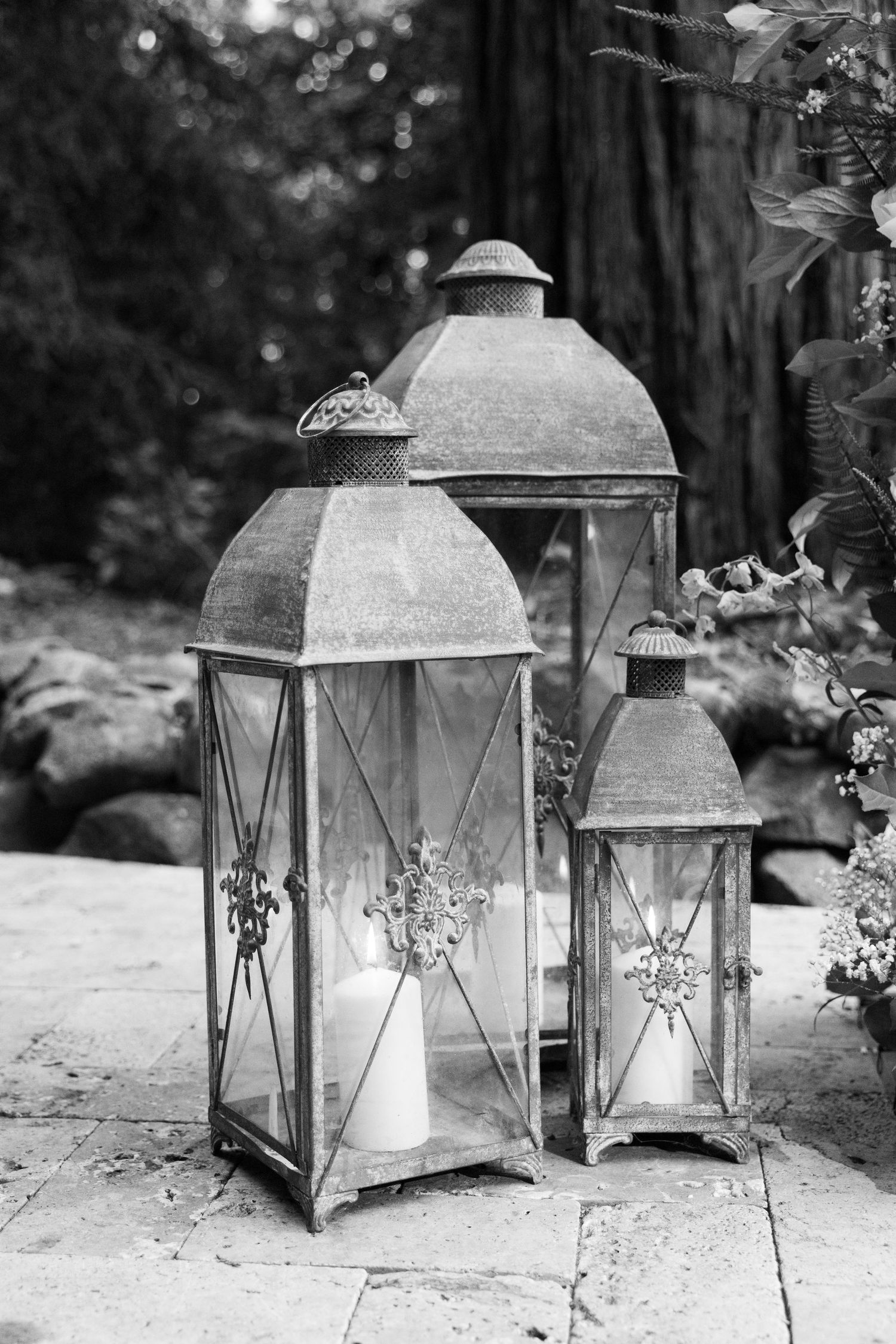 A collection of vintage metal lanterns with glass panels arranged in a rustic outdoor setting with soft bokeh background.