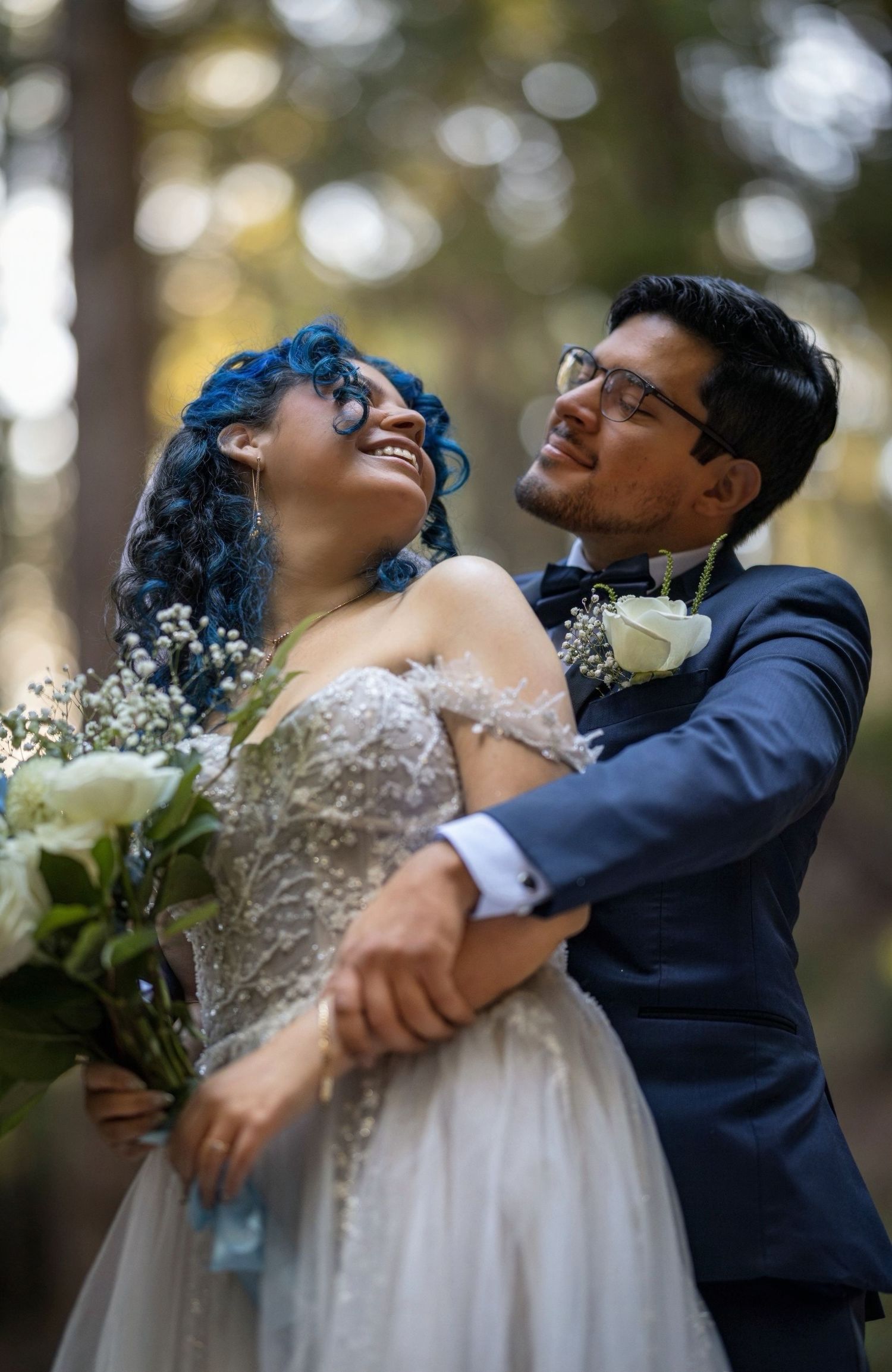 A joyful wedding couple embraces and laughs together in a romantic outdoor setting with soft bokeh lighting.