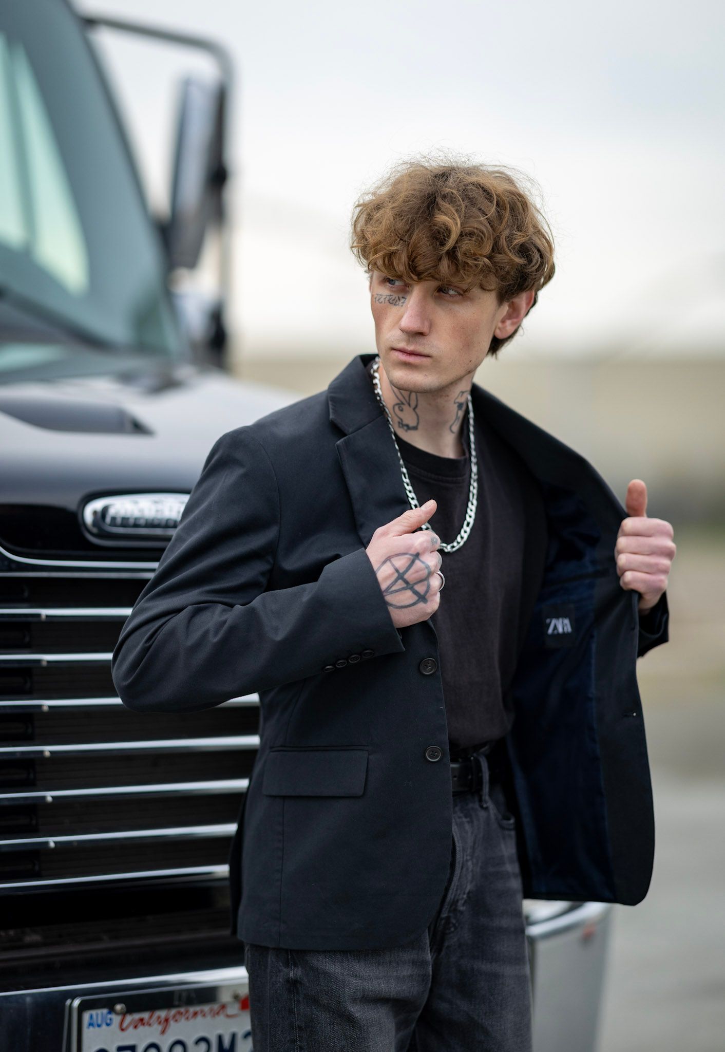 A person in a black coat smoking a cigarette while walking past a parked car.