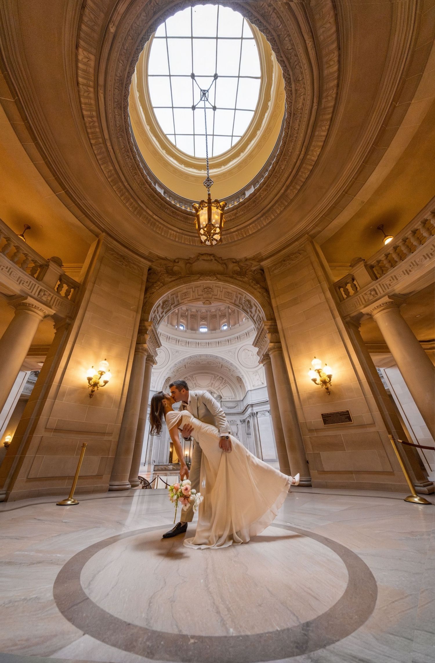 Couple sharing a romantic dip kiss under the grand rotunda of San Francisco City Hall on their wedding day.