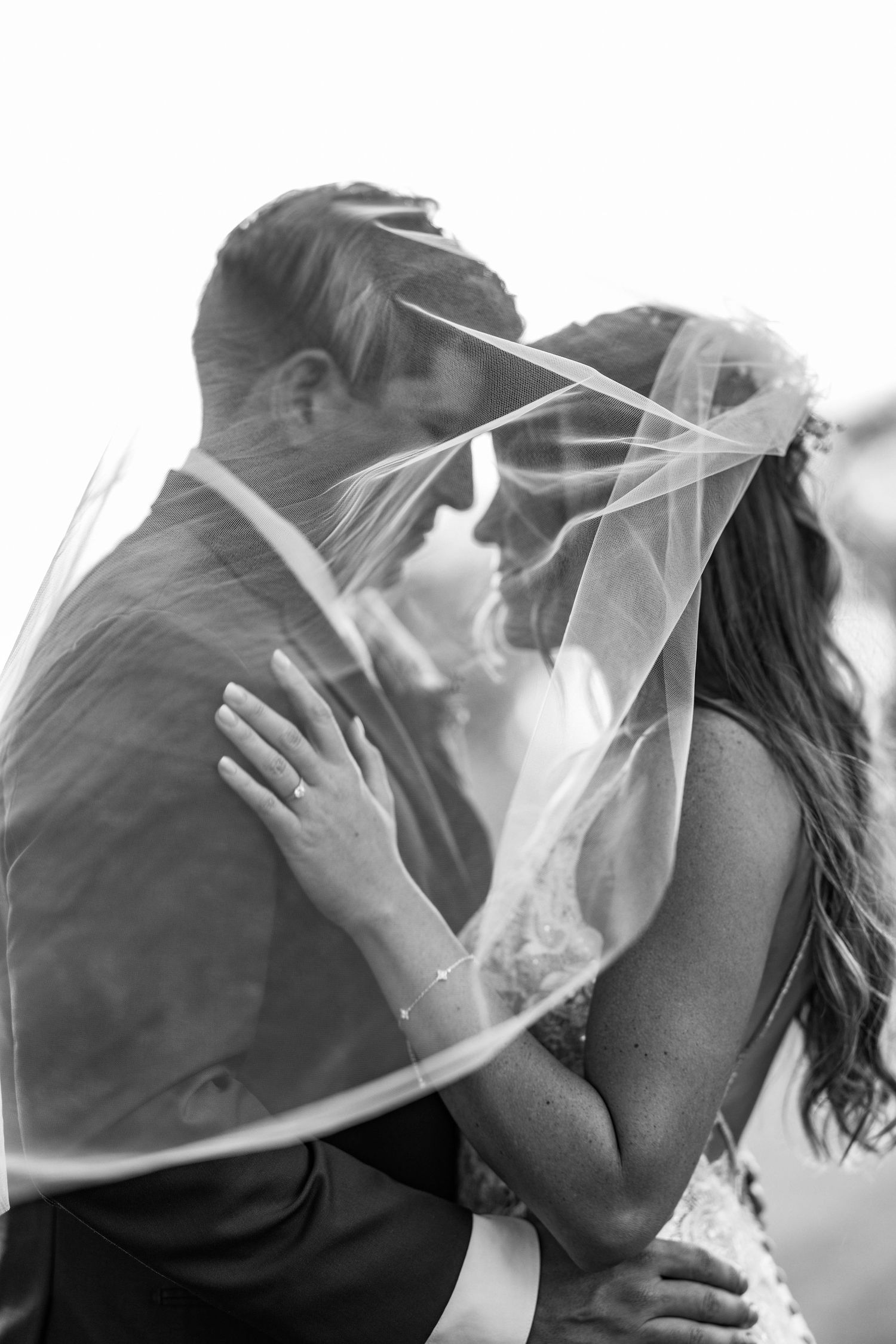 A romantic black and white photo series showing four intimate wedding kisses between newlyweds under a flowing veil.
