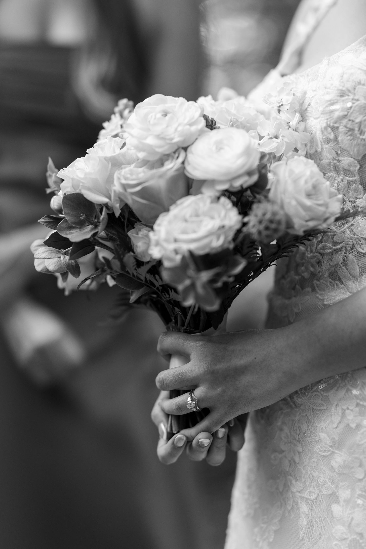 Black and white photo of a bride holding a bouquet of roses, wearing a diamond engagement ring and lace wedding dress.