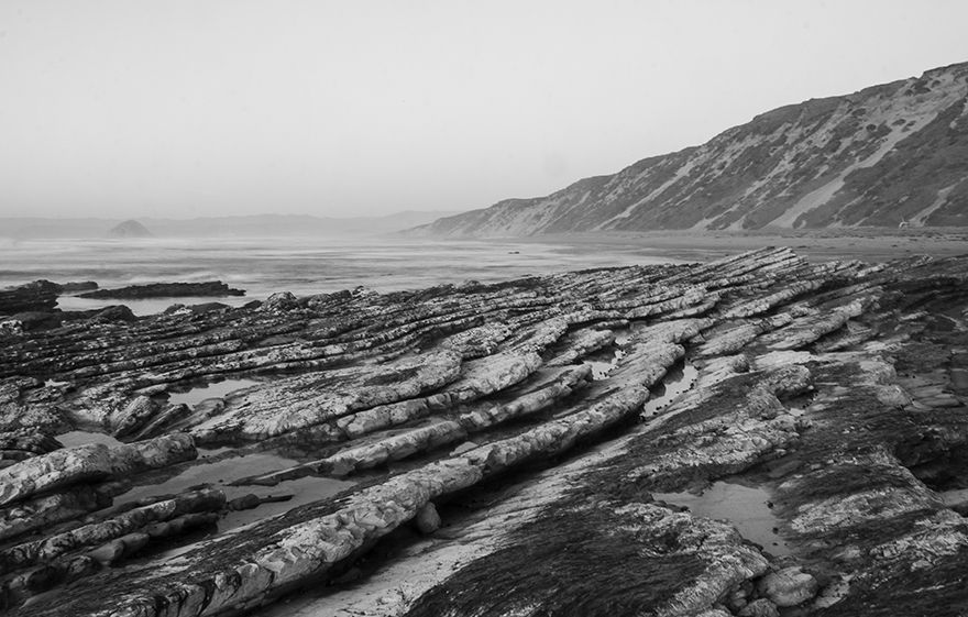 Dramatic black and white panoramic view of rugged coastal cliffs and rock formations along a misty shoreline.