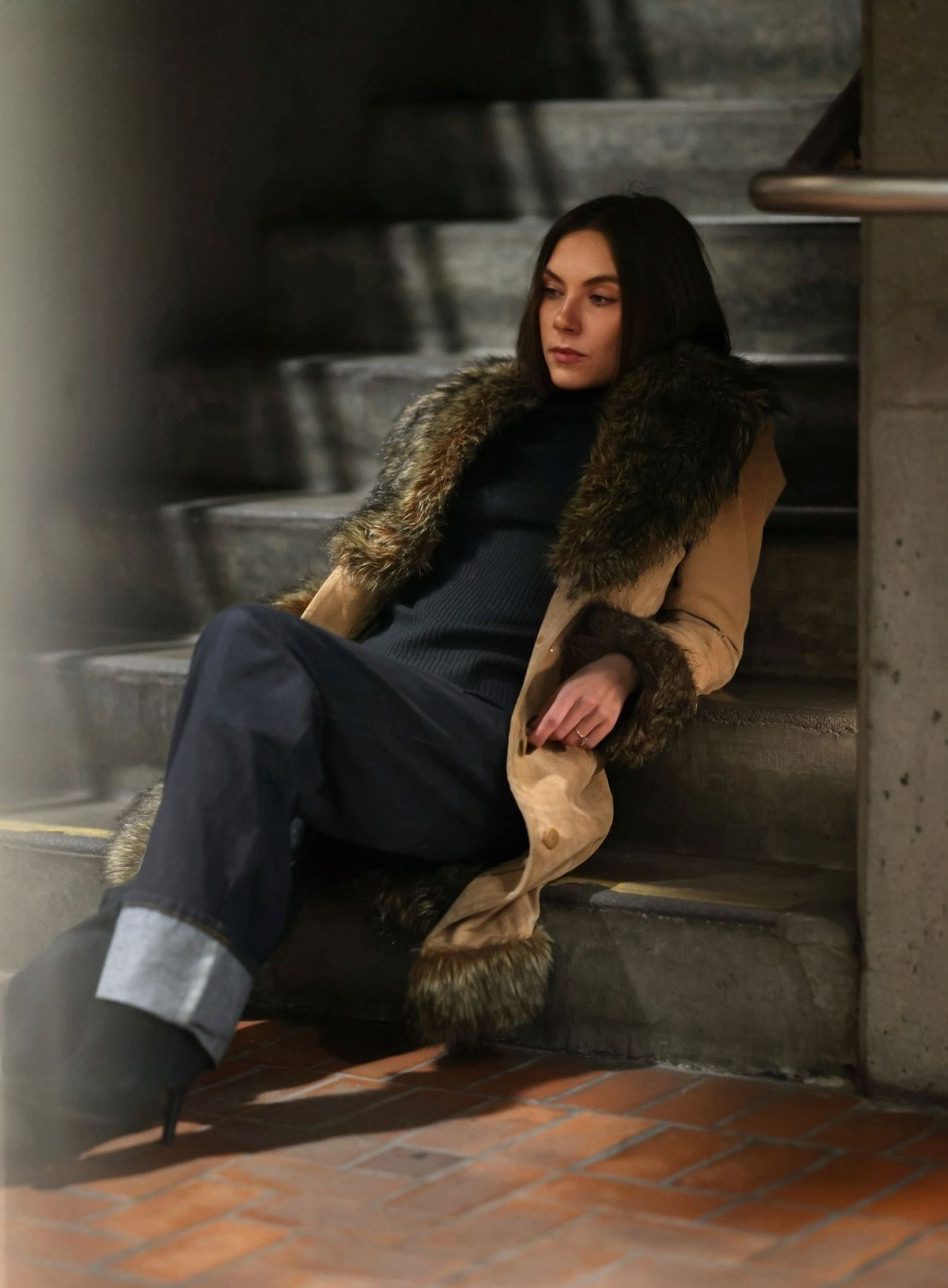 Person in casual attire reclining on concrete steps in moody lighting.
