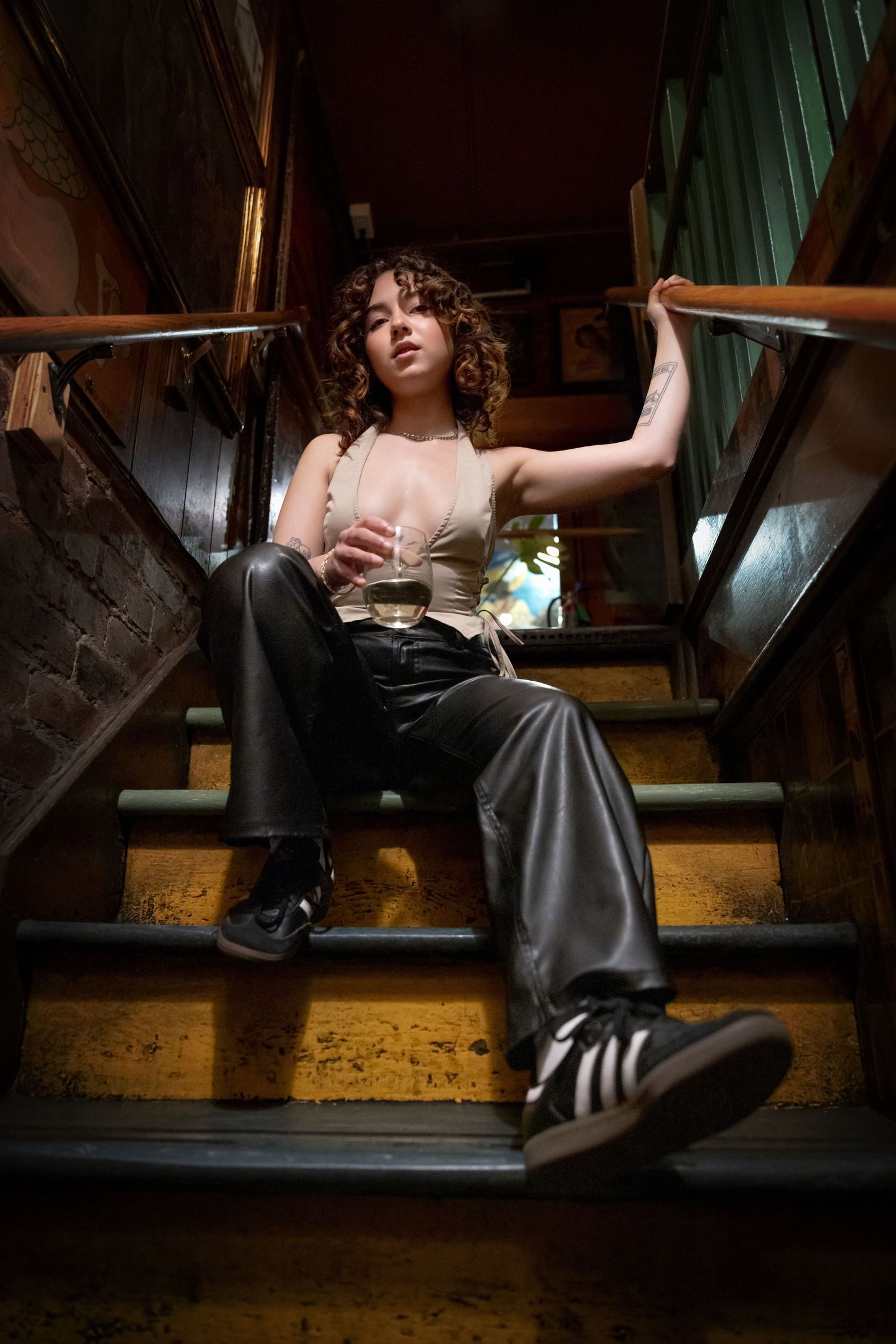 A person sits on wooden stairs in dark clothing and boots, creating a moody atmospheric composition.