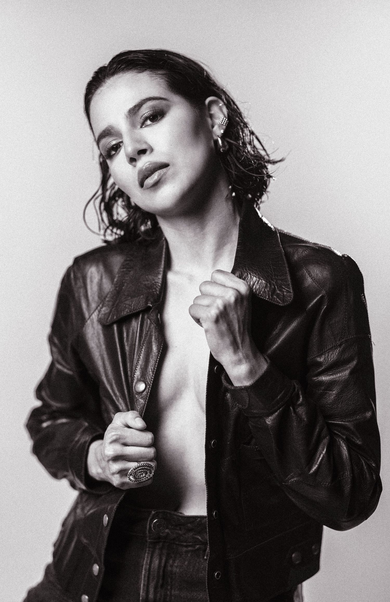 Black and white portrait of a young woman in a leather jacket, posing confidently against a light background.