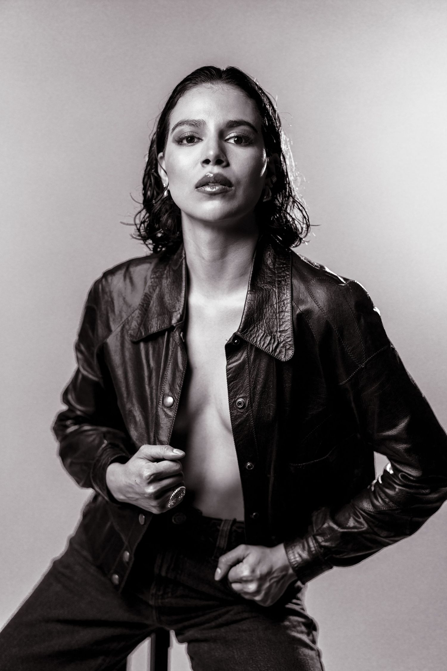 Black and white portrait of a woman in an open leather jacket and jeans, posing confidently in a studio.