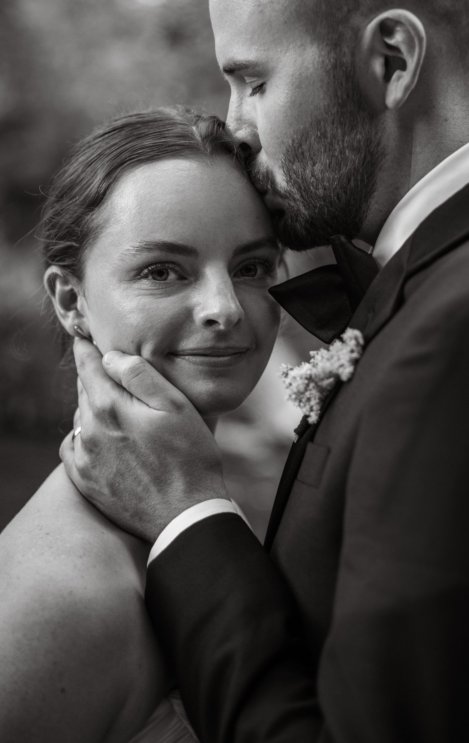 Black and white wedding photo of groom kissing bride on forehead while tenderly holding her face.