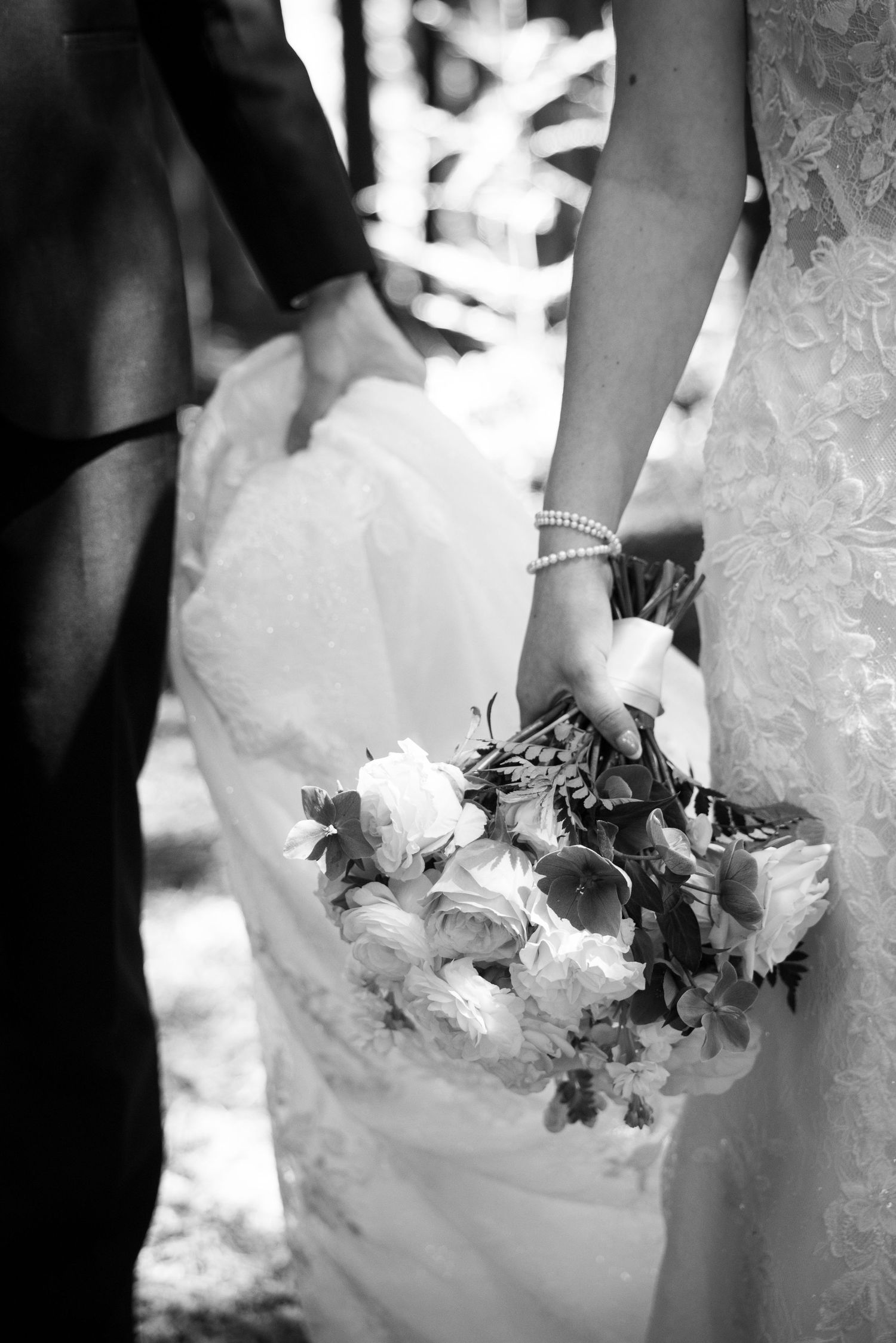 Black and white photo of bride holding floral bouquet with groom at wedding ceremony.