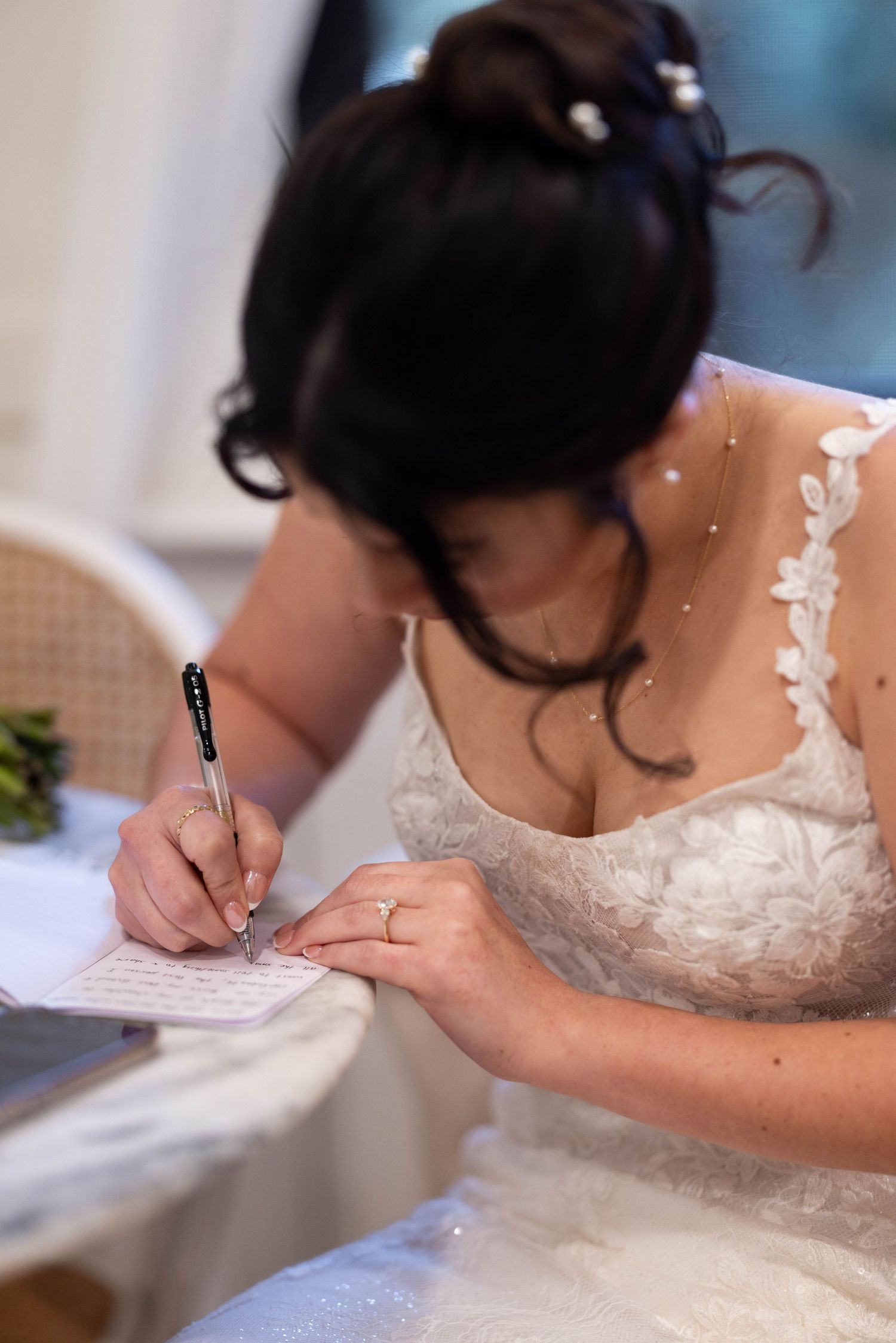 Bride in lace wedding dress signing marriage certificate at reception table with pen.