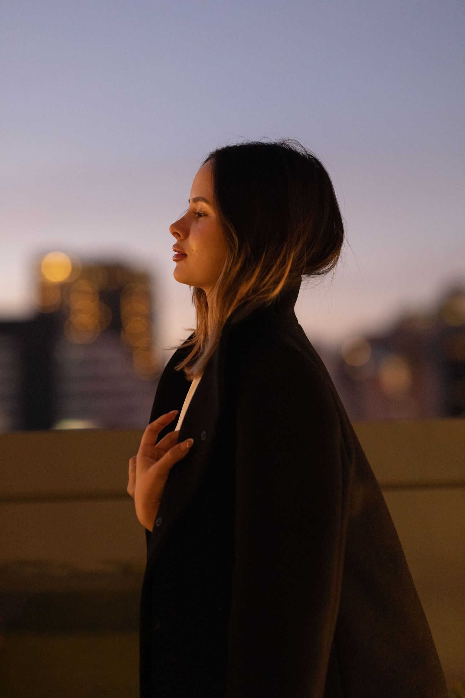 Silhouette of person in black coat against sunset city skyline with warm bokeh lights in background.
