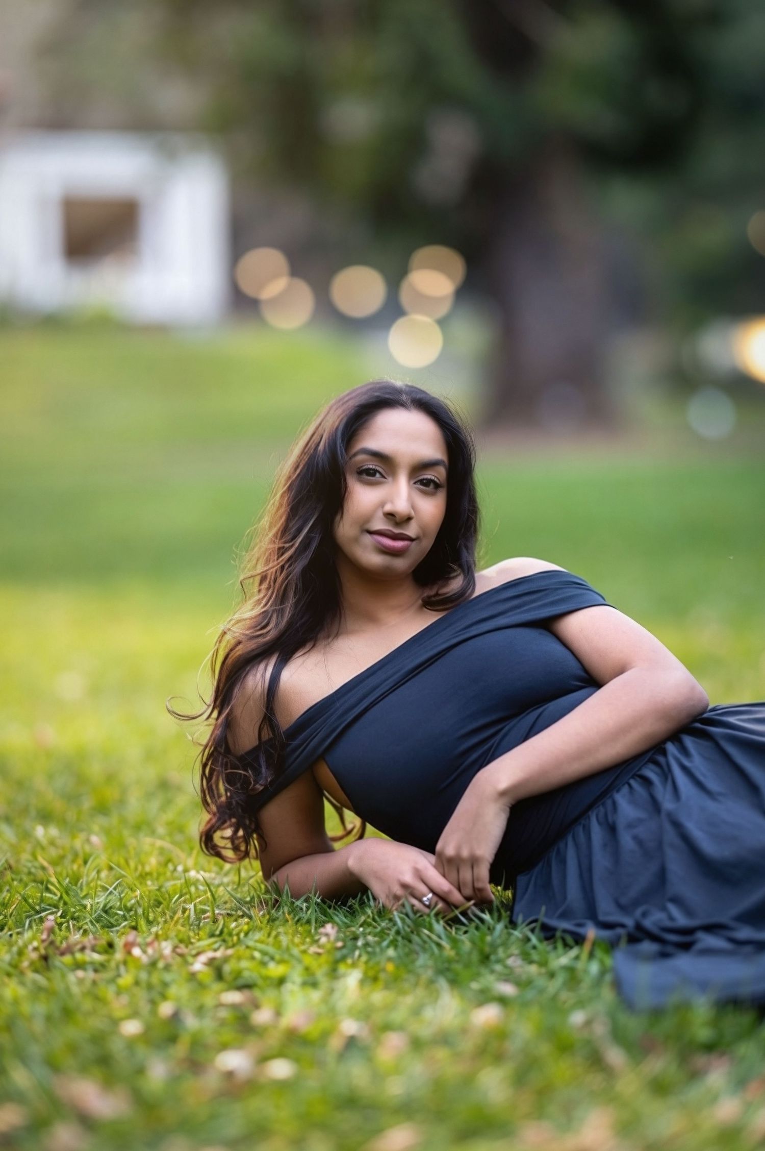 A person in a black outfit reclines on green grass with soft bokeh lights in the background.