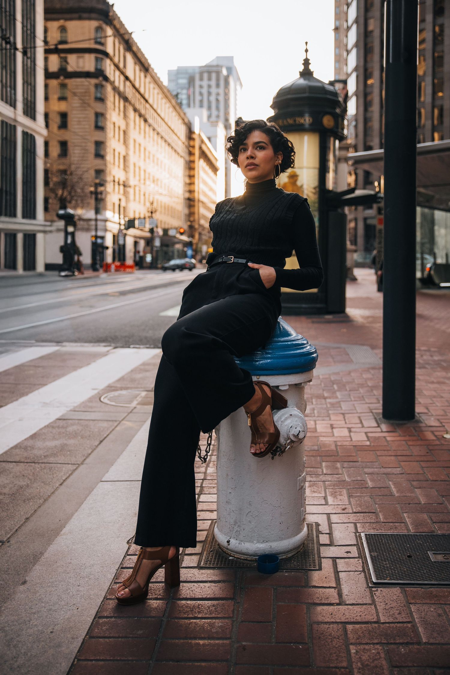 Two people embrace on a brick sidewalk in front of historic urban buildings during golden hour.
