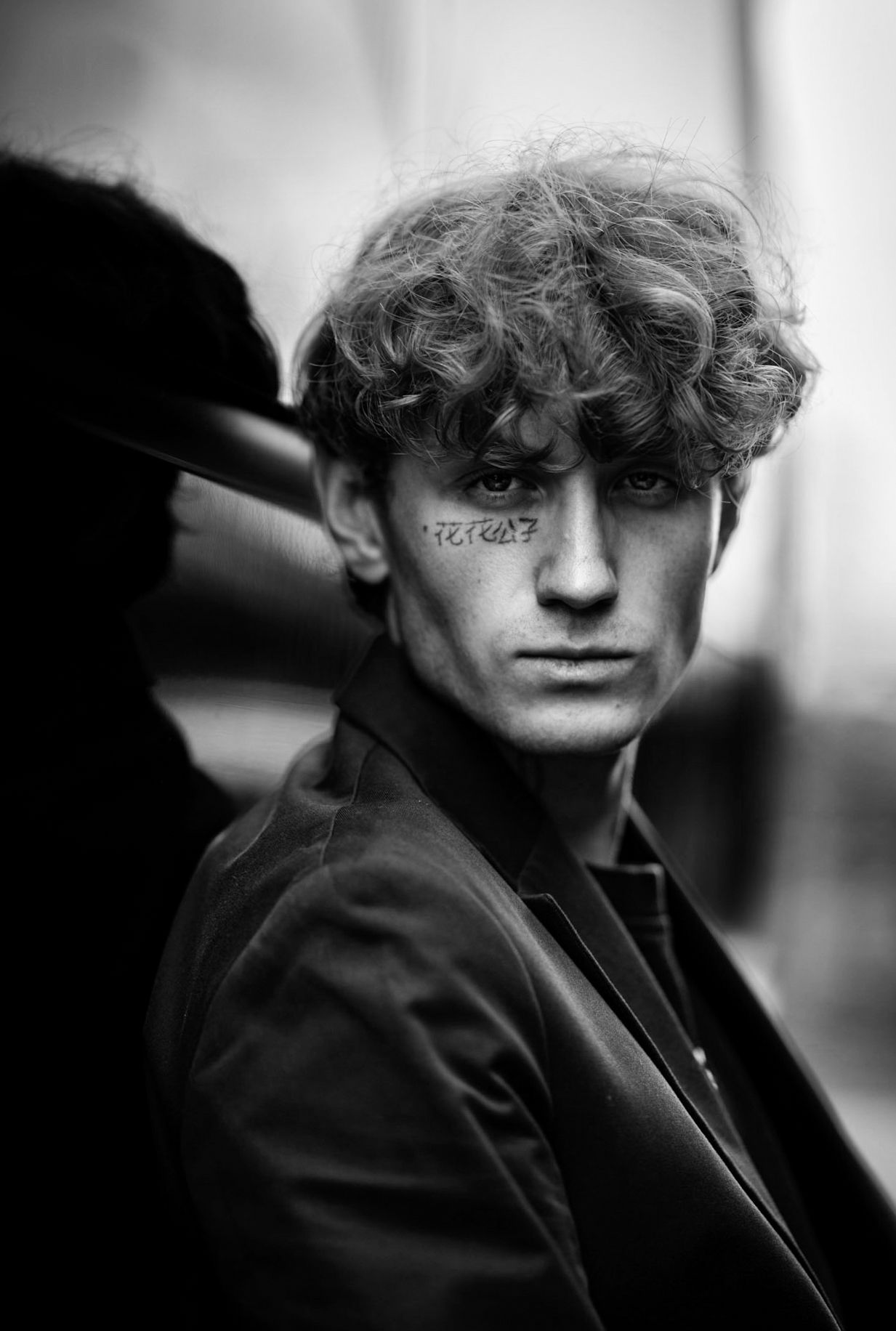 A series of black and white artistic portraits showing a figure in a dark jacket with curly hair against a blurred background.
