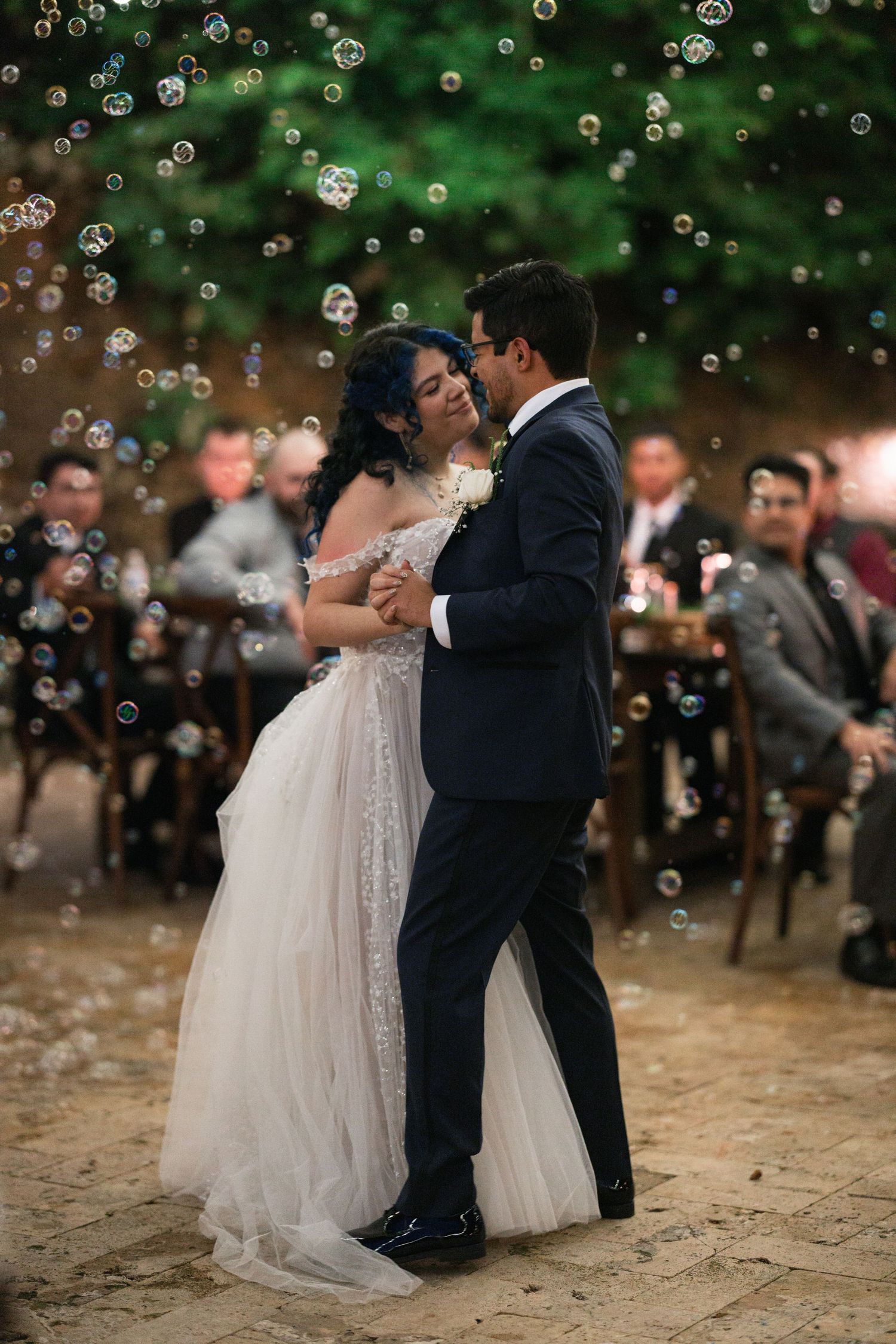 A couple shares their first dance at an outdoor wedding reception as bubbles float through the air around them.